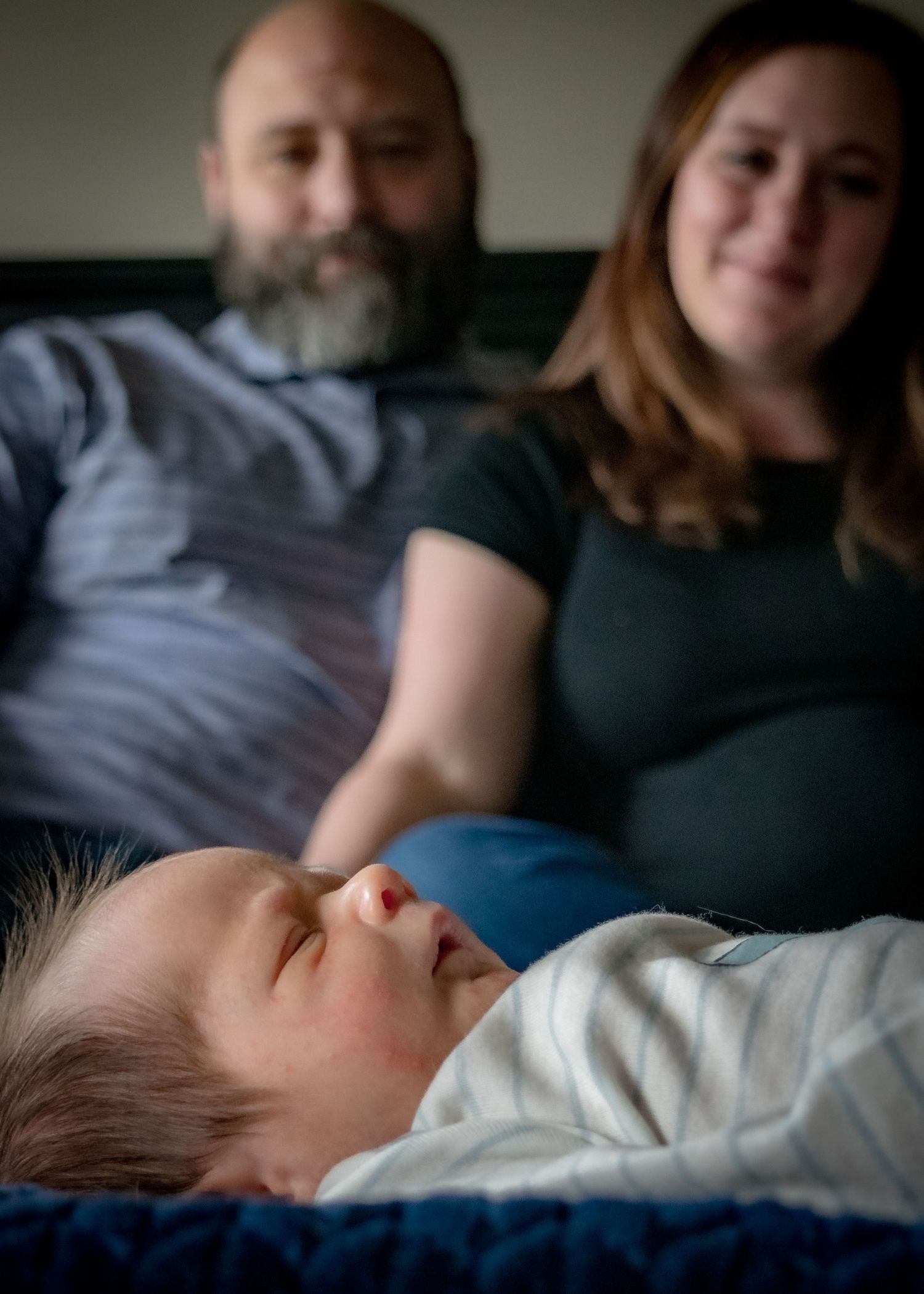 Smiling parents sitting together watching their peaceful sleeping newborn baby.