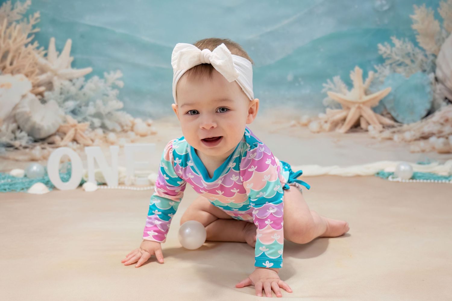 Baby girl in mermaid swimsuit crawling during ocean-themed first birthday photoshoot.