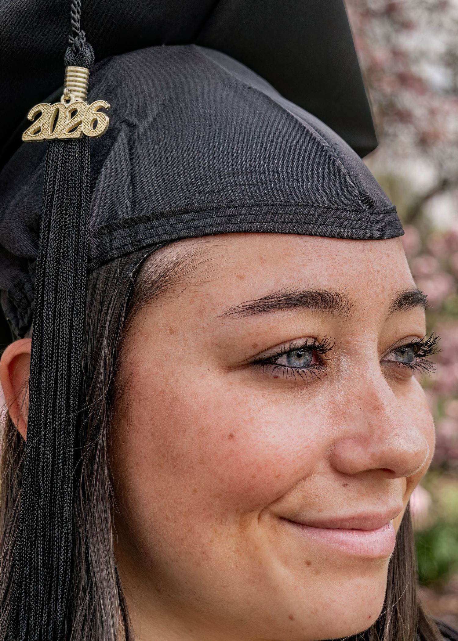 Close-up portrait of smiling female graduate wearing black cap with gold 2026 tassel charm.