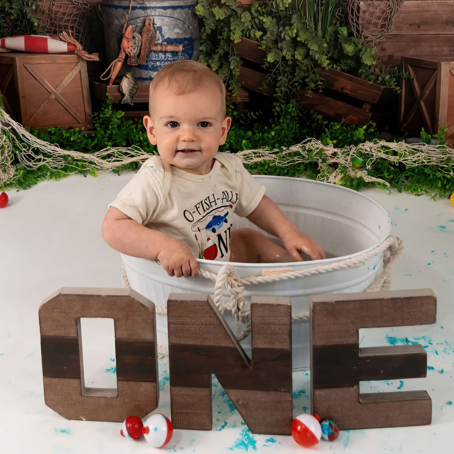 Adorable baby sits in metal tub beside wooden ONE sign at fishing-themed first birthday cake smash session.