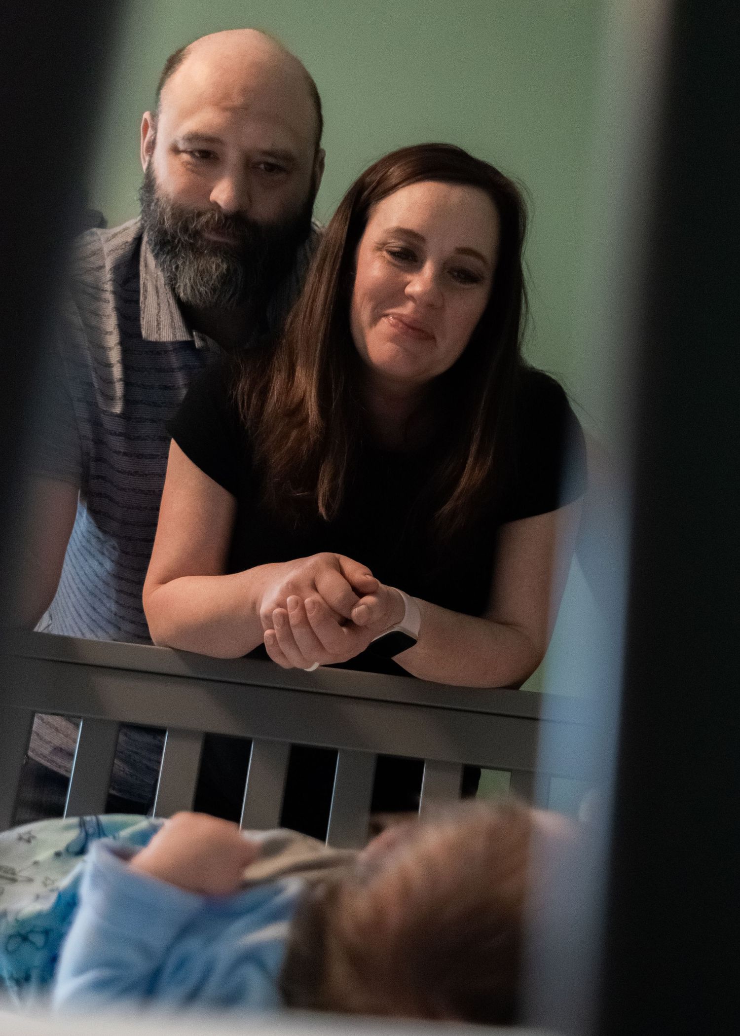 Parents lovingly watch their newborn baby sleeping in a crib.