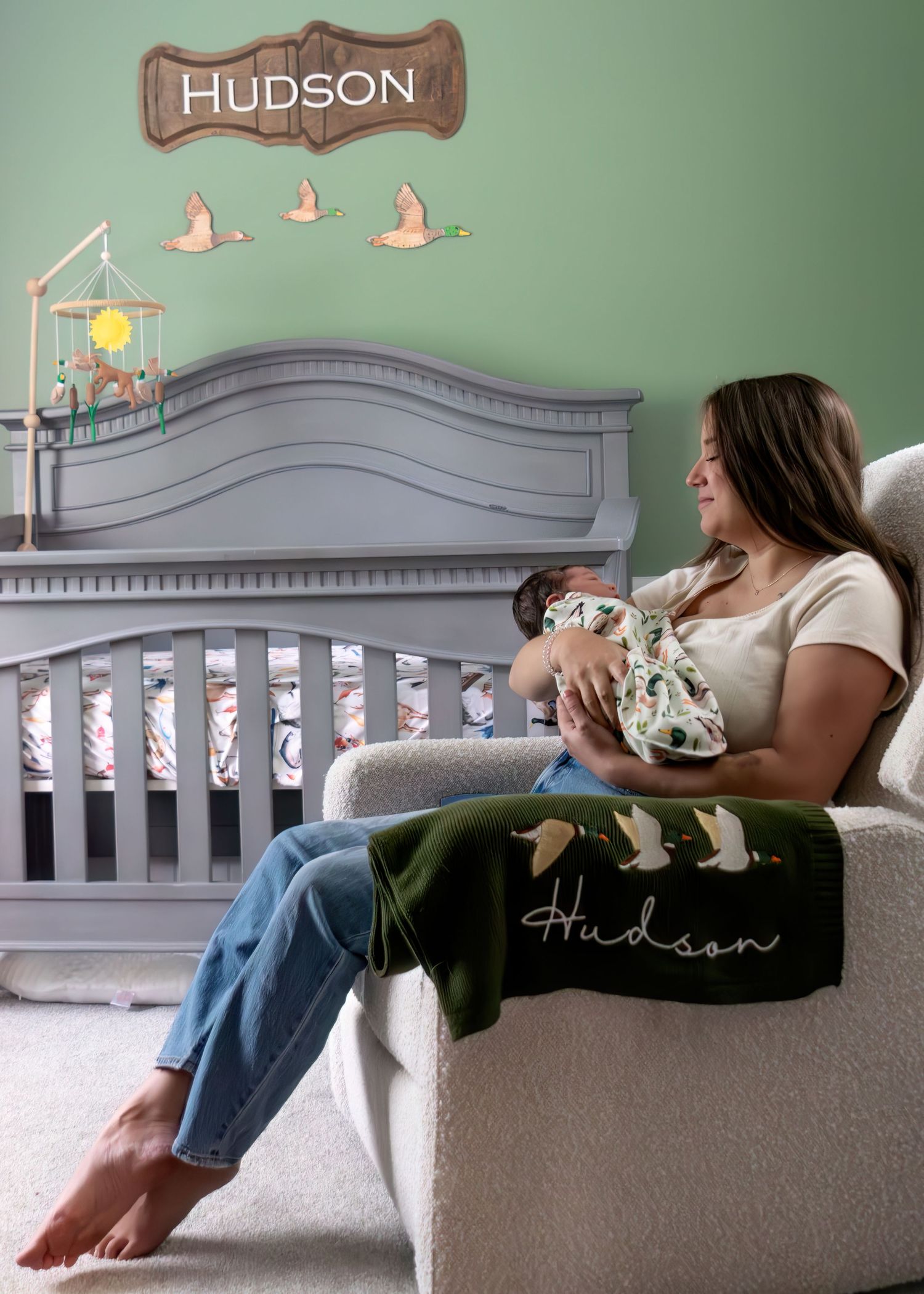 New mother nursing baby Hudson in nursery rocker with personalized name sign and duck mobile.