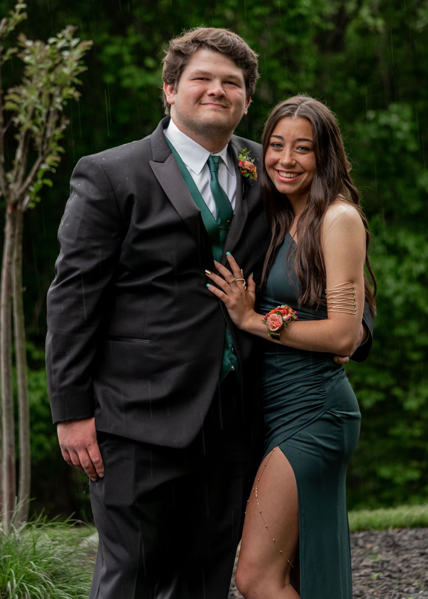 Couple posing in formal prom attire, man in black suit and woman in emerald green gown.