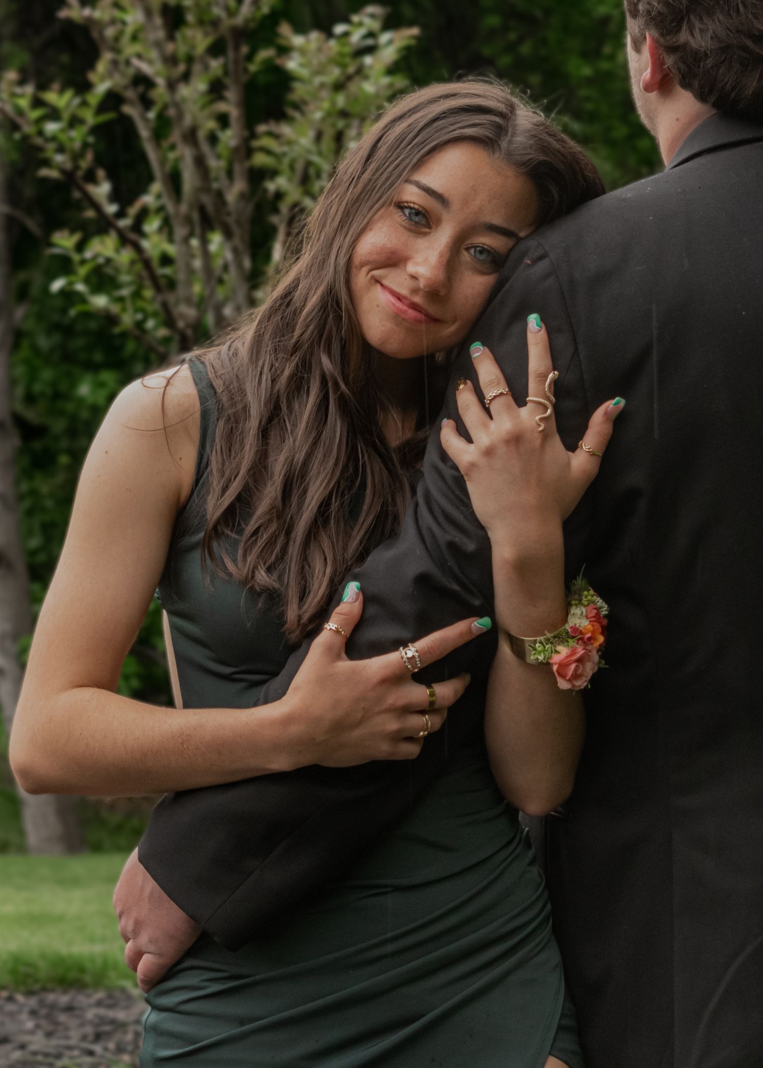 Young woman in dark green dress smiling while embracing a man in a black suit.
