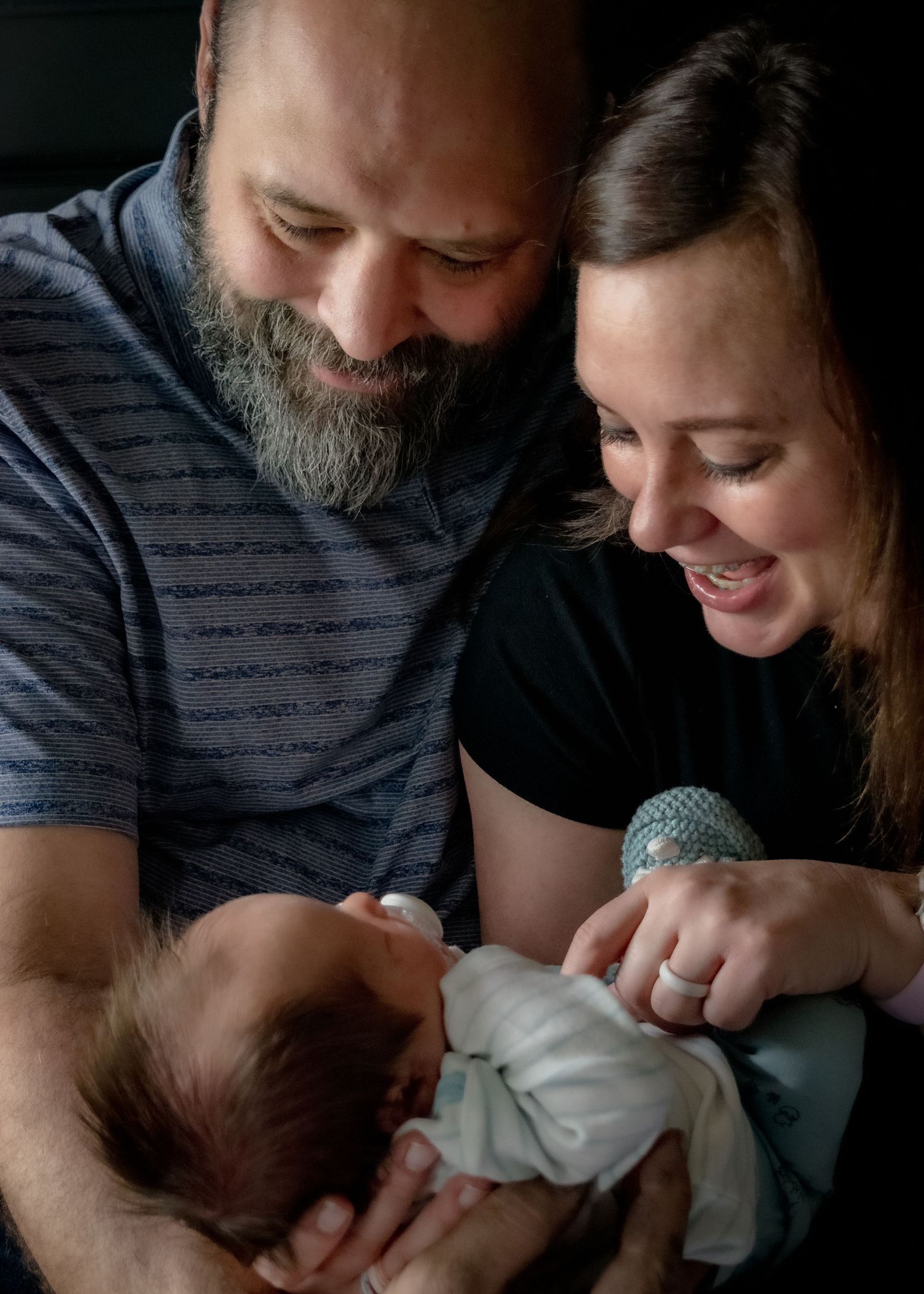 Happy parents smiling and holding their newborn baby together.