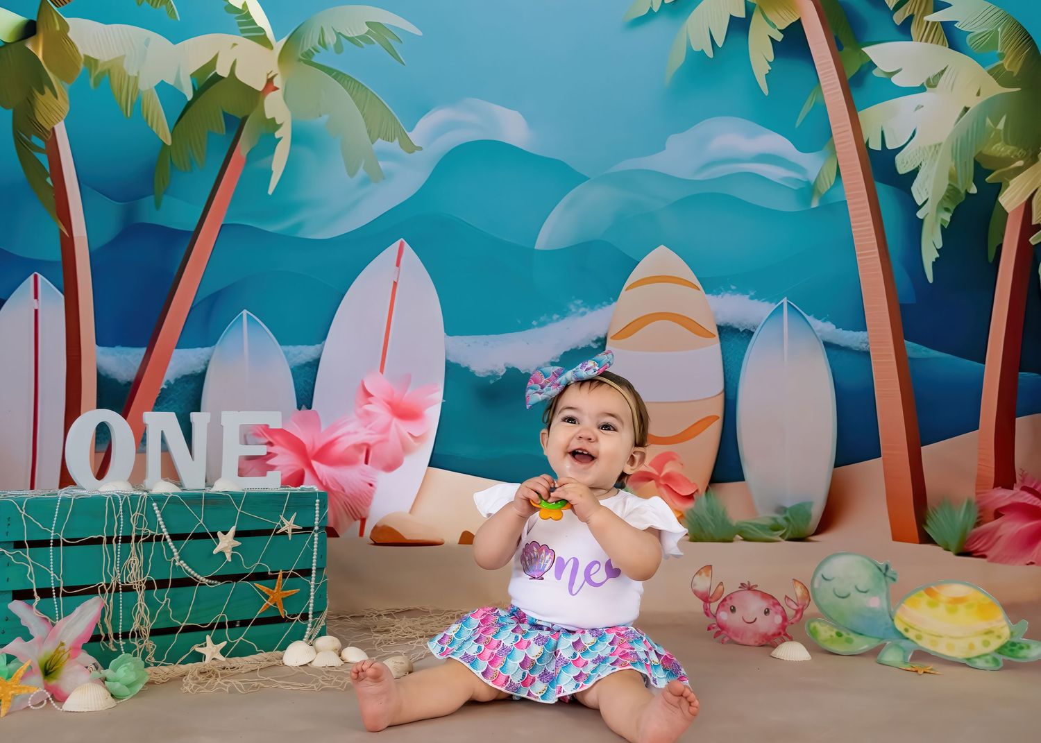 Baby girl in floral outfit celebrates first birthday at beach-themed cake smash with surfboards and palm trees.
