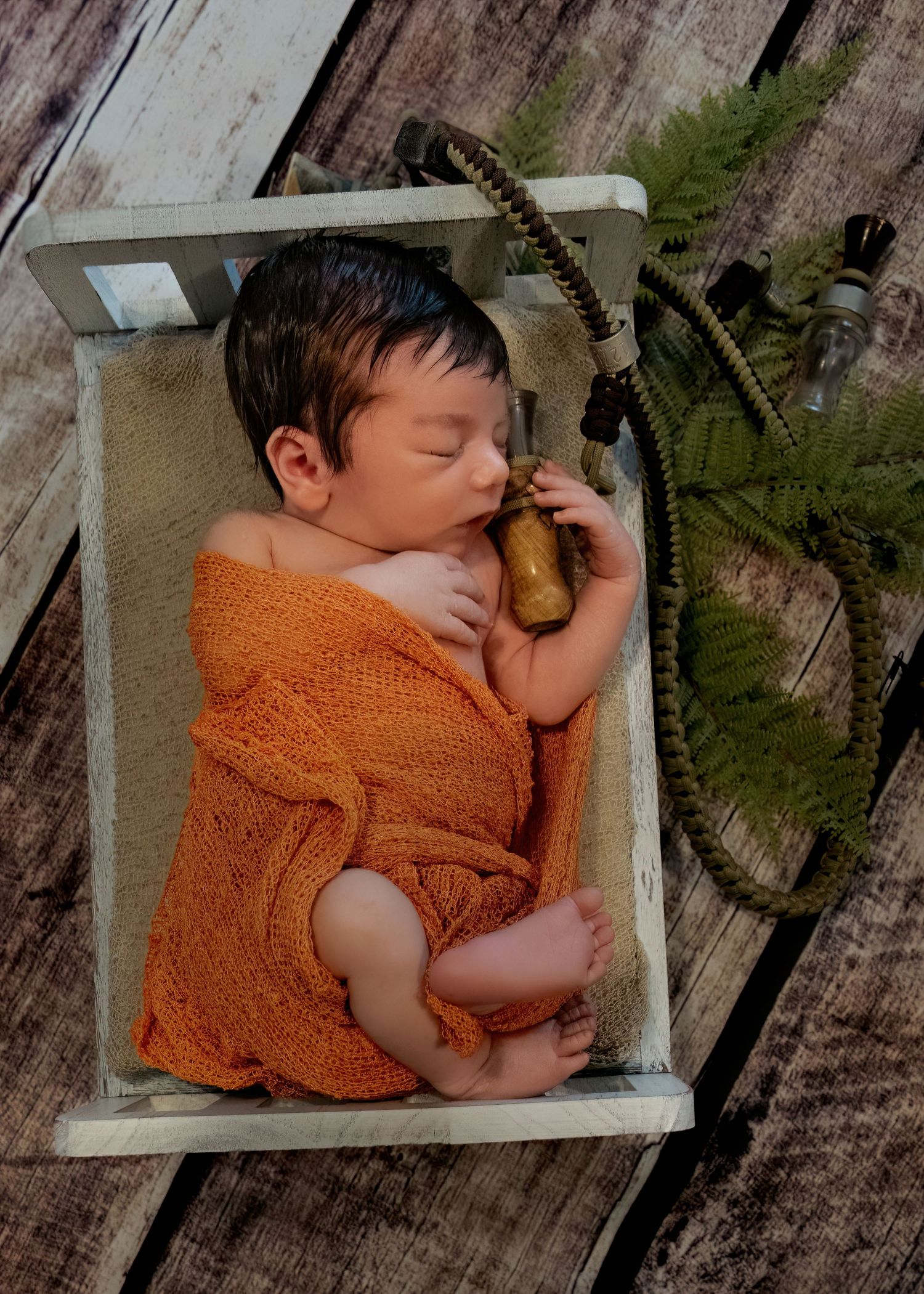 Sleeping newborn wrapped in orange knit blanket in tiny wooden bed with fishing theme props.