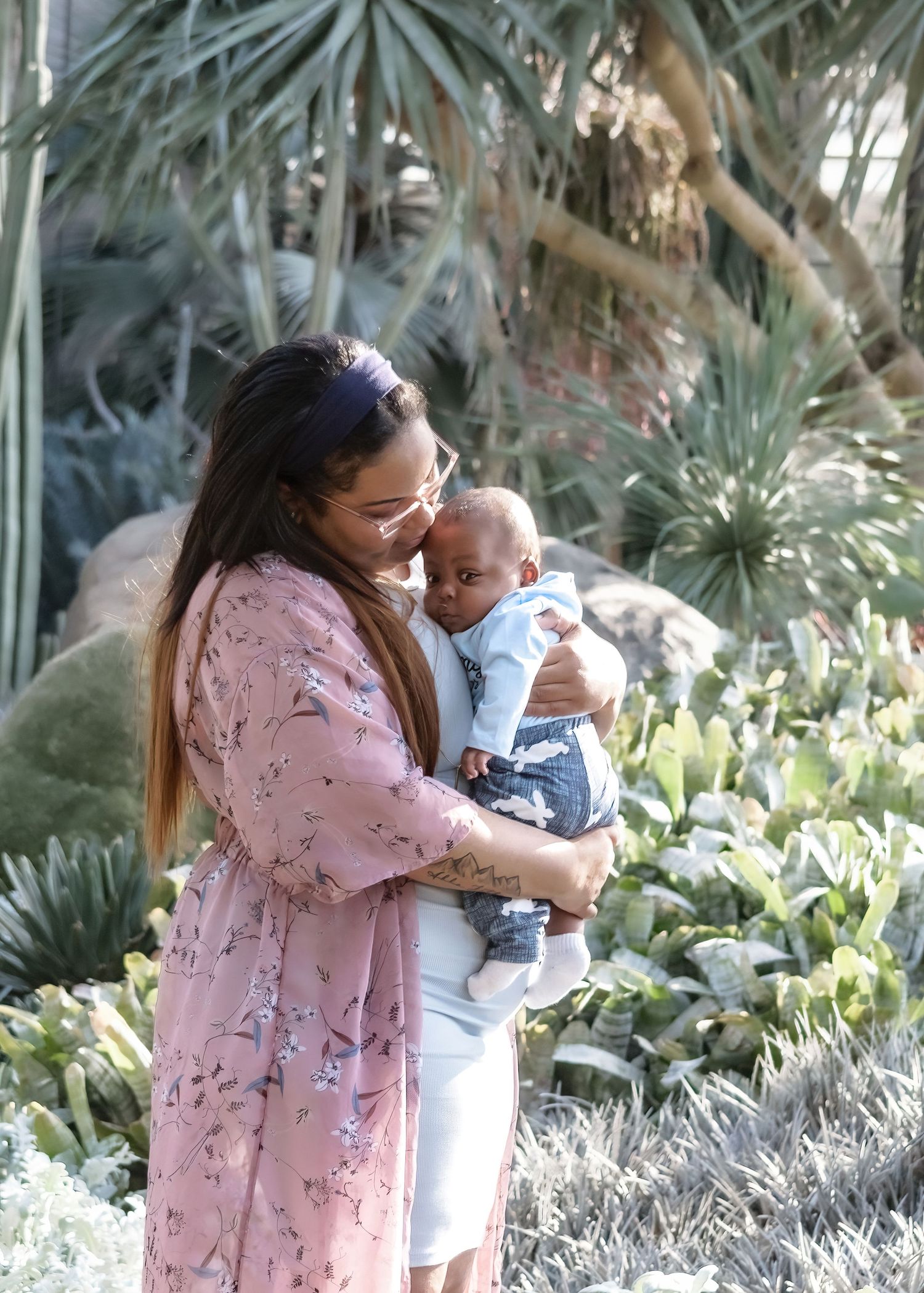 Loving mother in pink floral kimono cradling her infant son in lush garden setting.