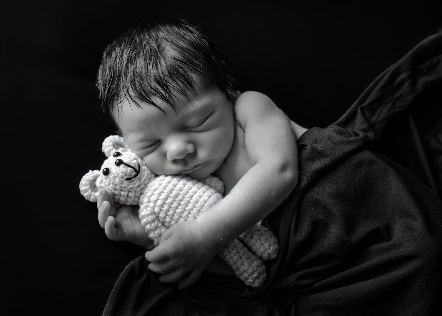 Sleeping newborn baby cuddling a knit teddy bear in black and white portrait photo.