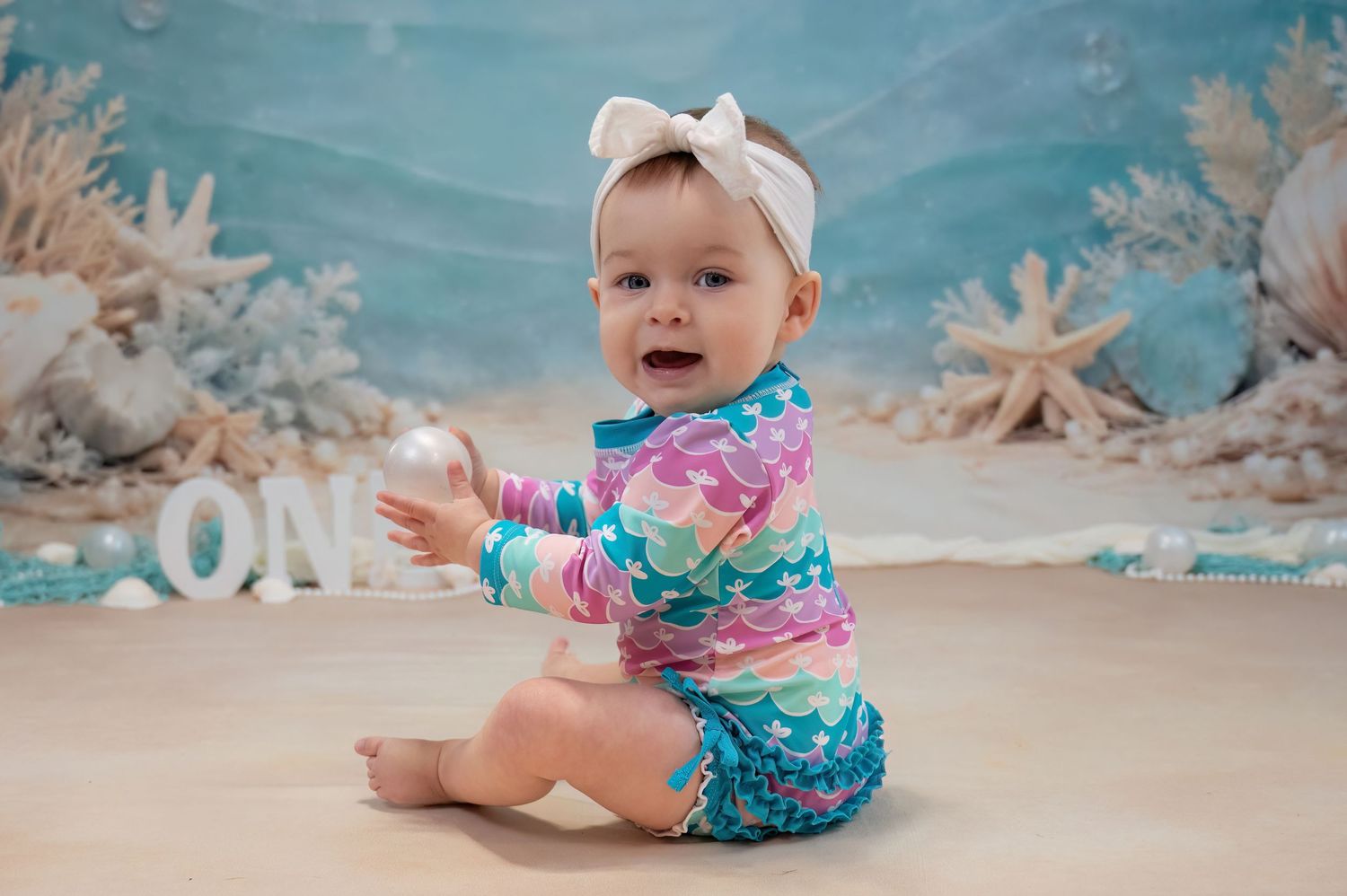 Happy baby in colorful mermaid outfit crawling at ocean-themed first birthday session.