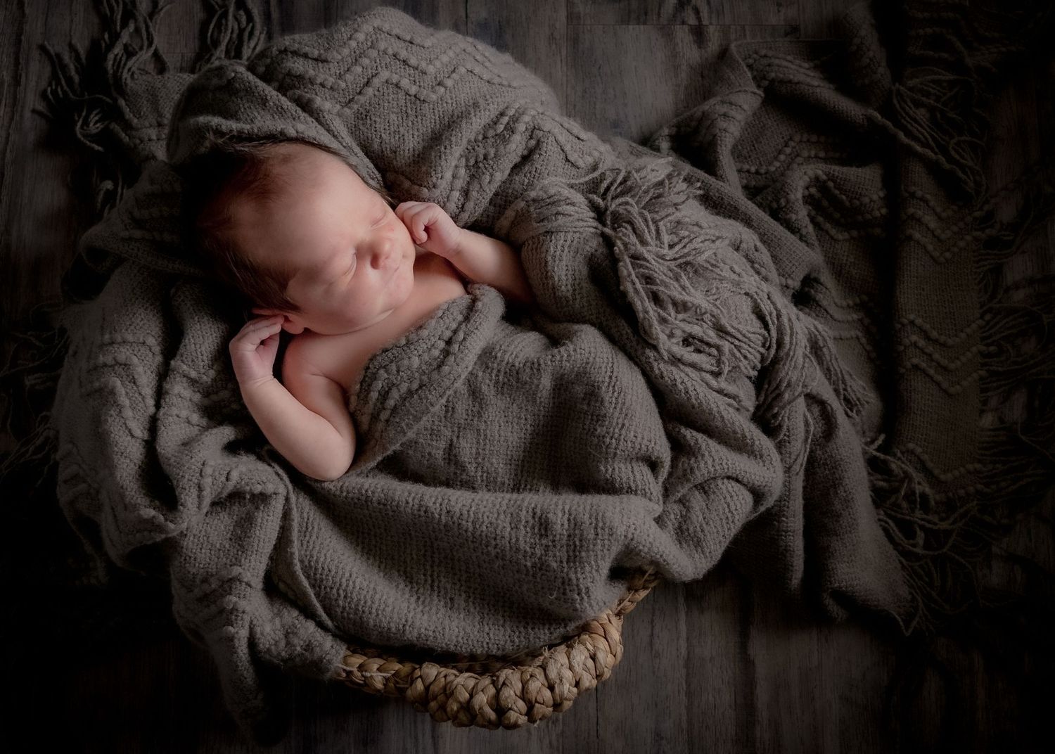 Sleeping newborn baby wrapped in a gray knit blanket in a basket.