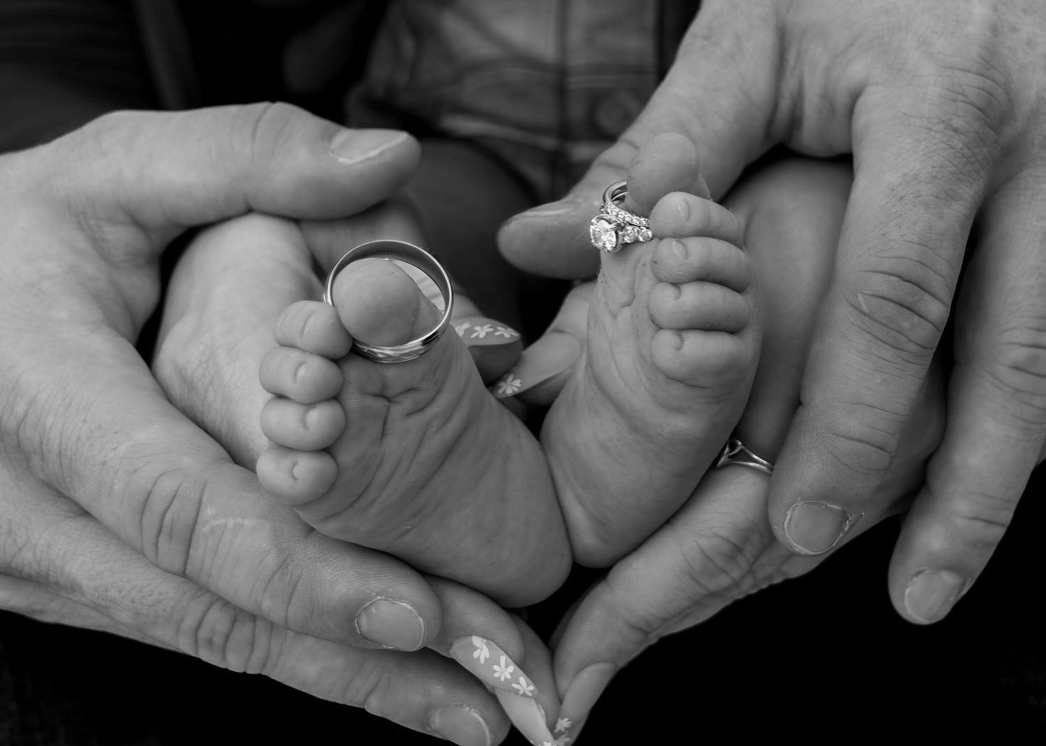 Black and white photo of newborn baby feet held by parents wearing wedding rings.