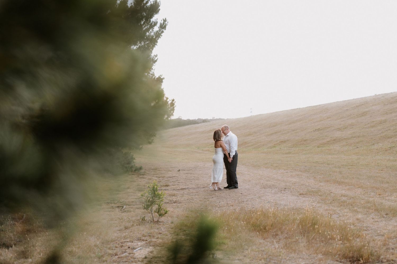 Silhouette of couple embracing on hilltop during golden hour.