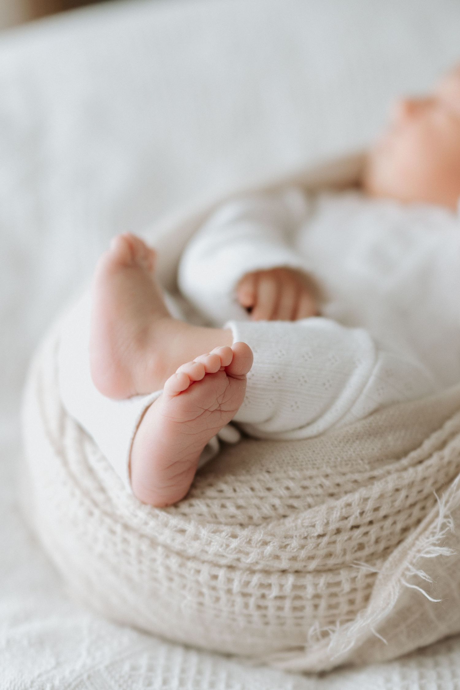 Close-up of tiny baby feet resting on white knitted blanket.