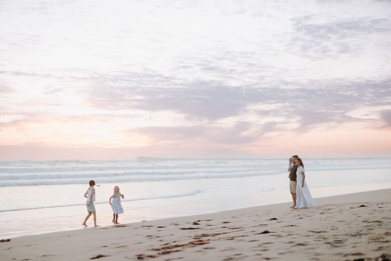 Couple walking on sandy beach at sunset with cascading views of silhouettes continuing into the horizon.