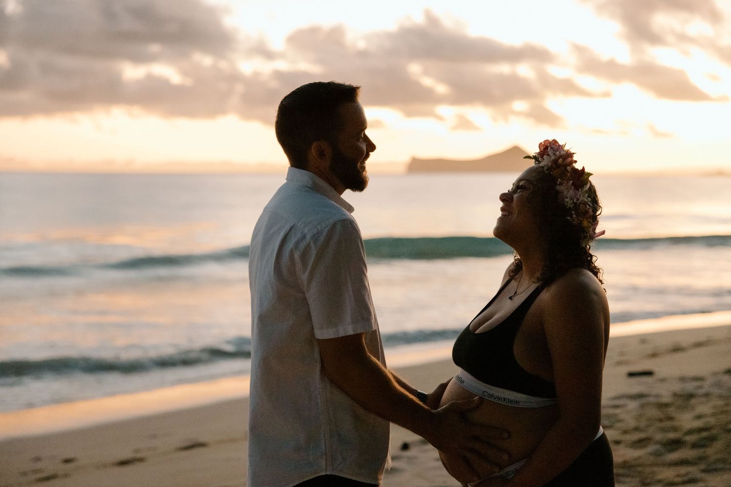 Silhouette of a couple sharing an intimate moment on the beach during sunset, with waves rolling in on the shore.