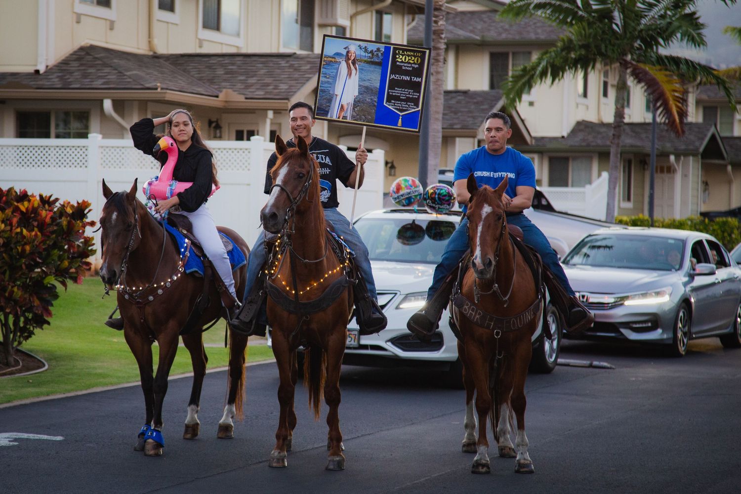 Three horseback riders parade through a residential street carrying flags and decorations.