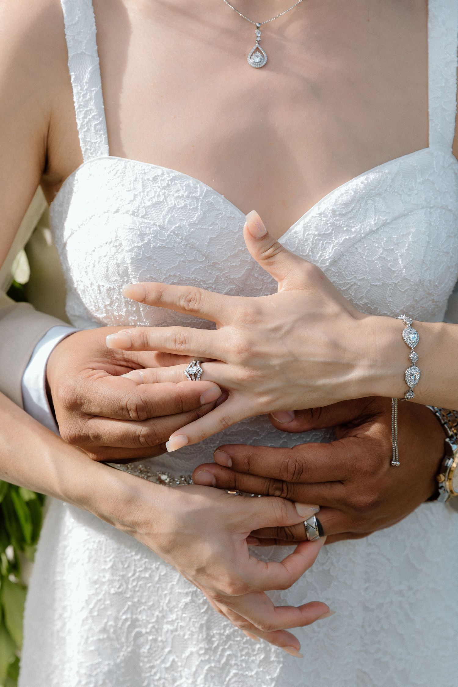 Close-up of hands with jewelry touching white lace wedding dress.