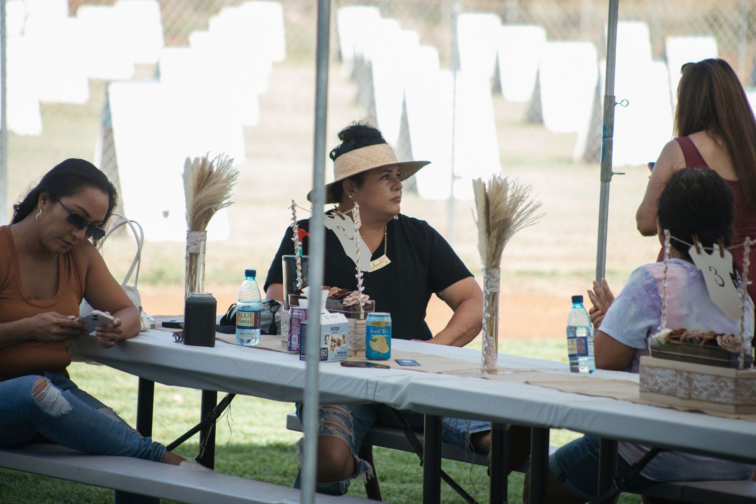 People gathered at a long picnic table outdoors sharing drinks and conversation.