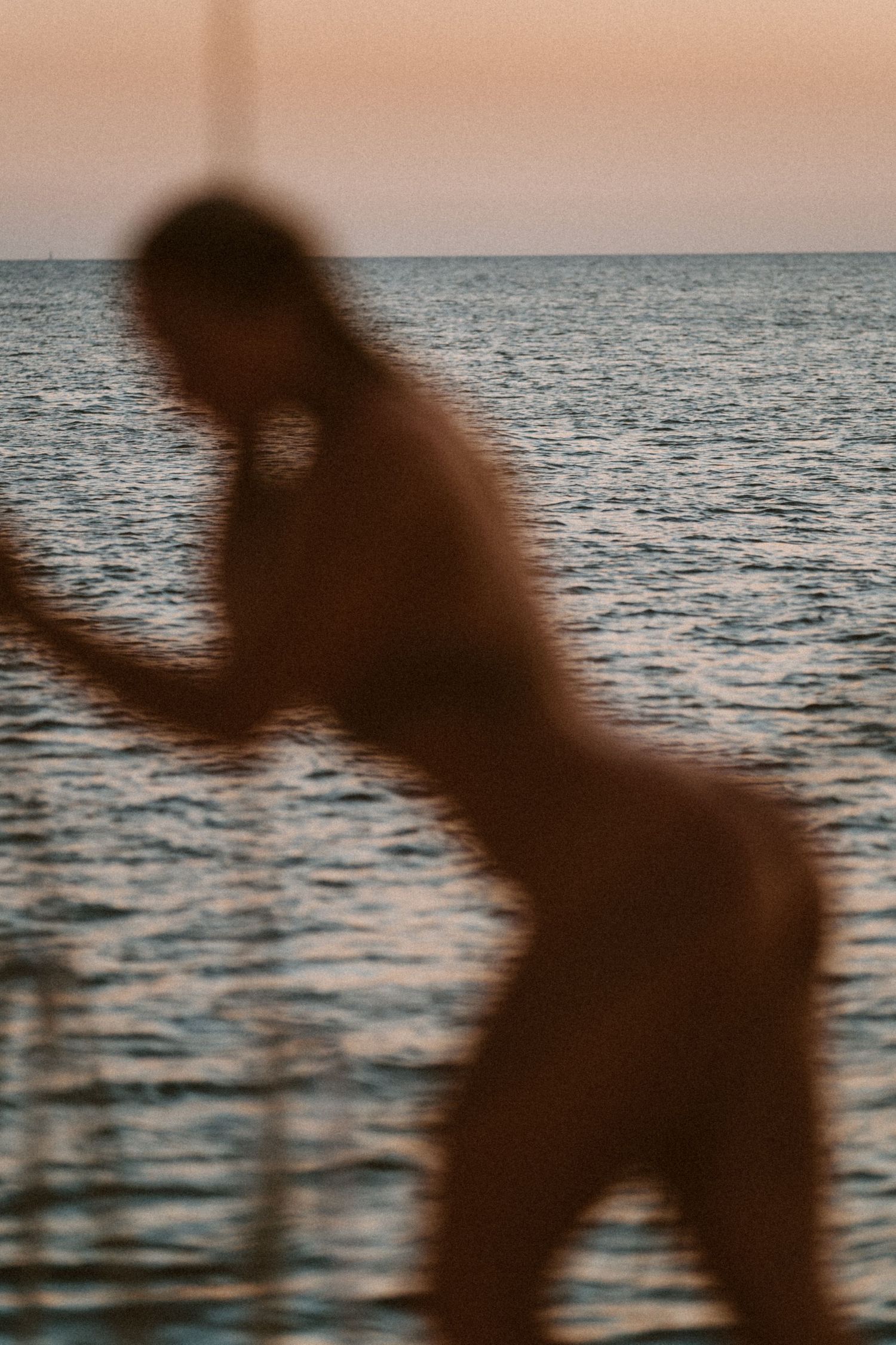 Silhouette against ocean horizon during sunset in artistic pose.