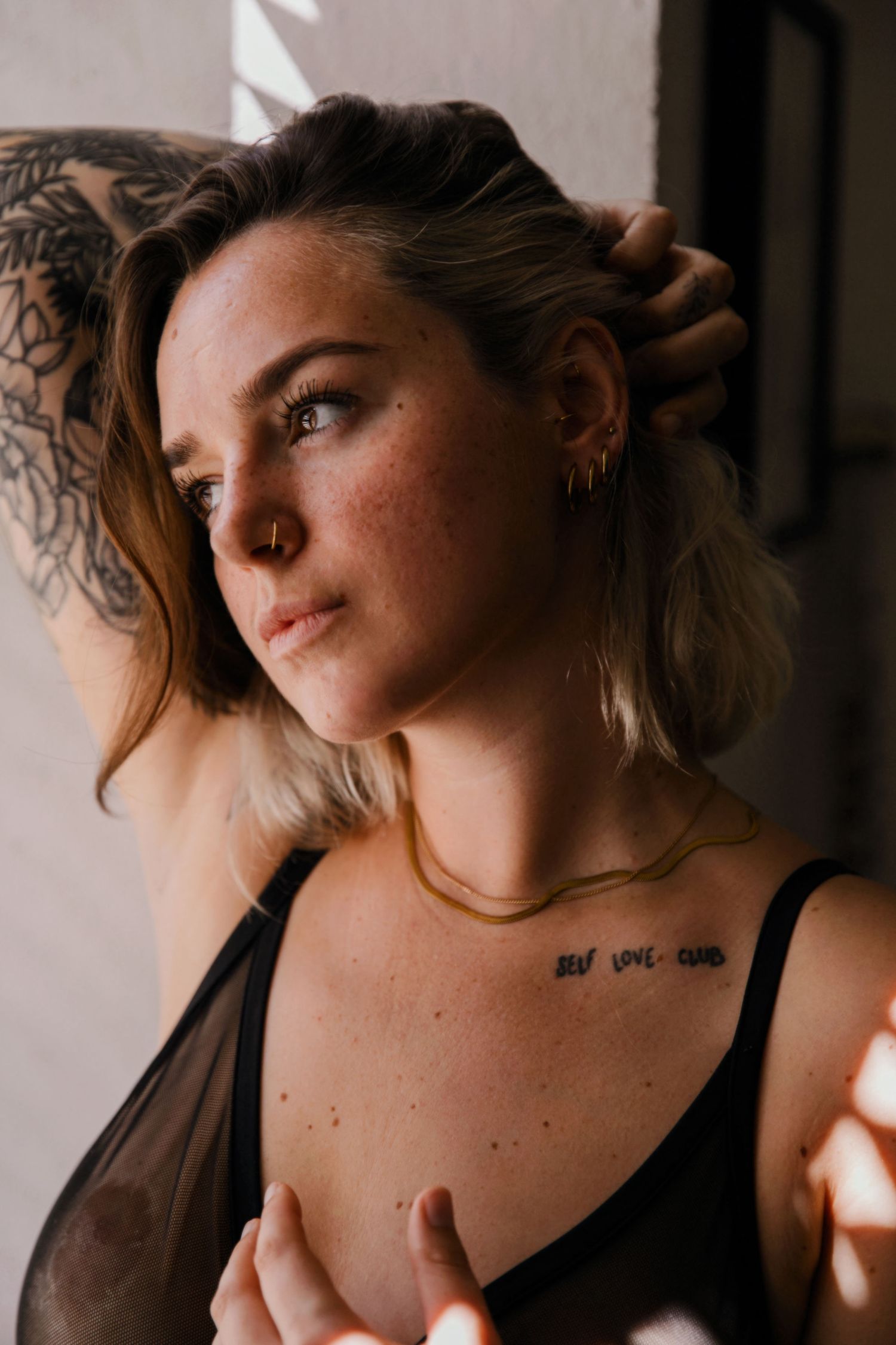 Portrait showing tattoo art and jewelry in natural window lighting.
