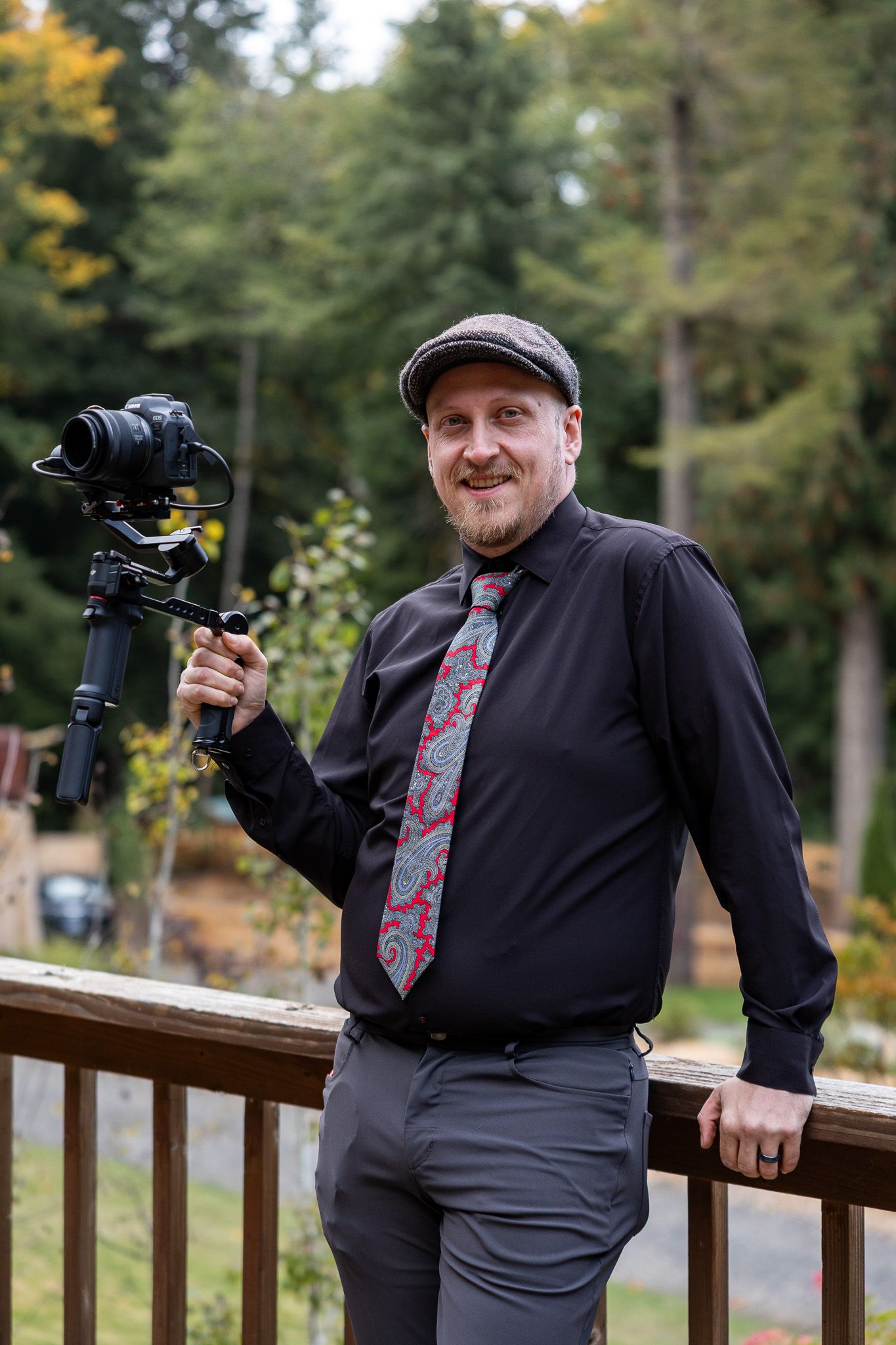 Videographer holding a camera gimbal stabilizer outdoors, wearing a black shirt and patterned tie.