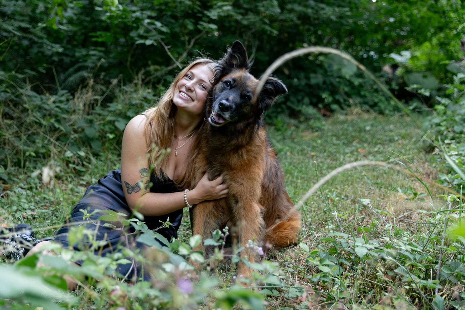 Happy woman embracing large brown dog while sitting in green grass outdoors.