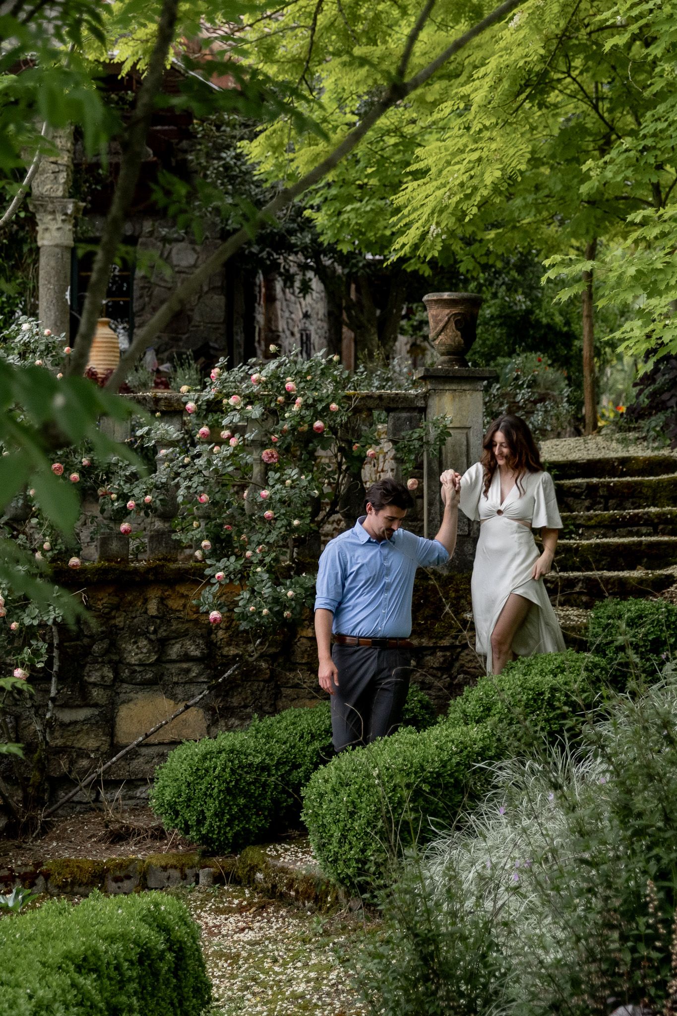 Couple walks through a lush garden with stone steps and blooming roses Villa Catalana Cellars.