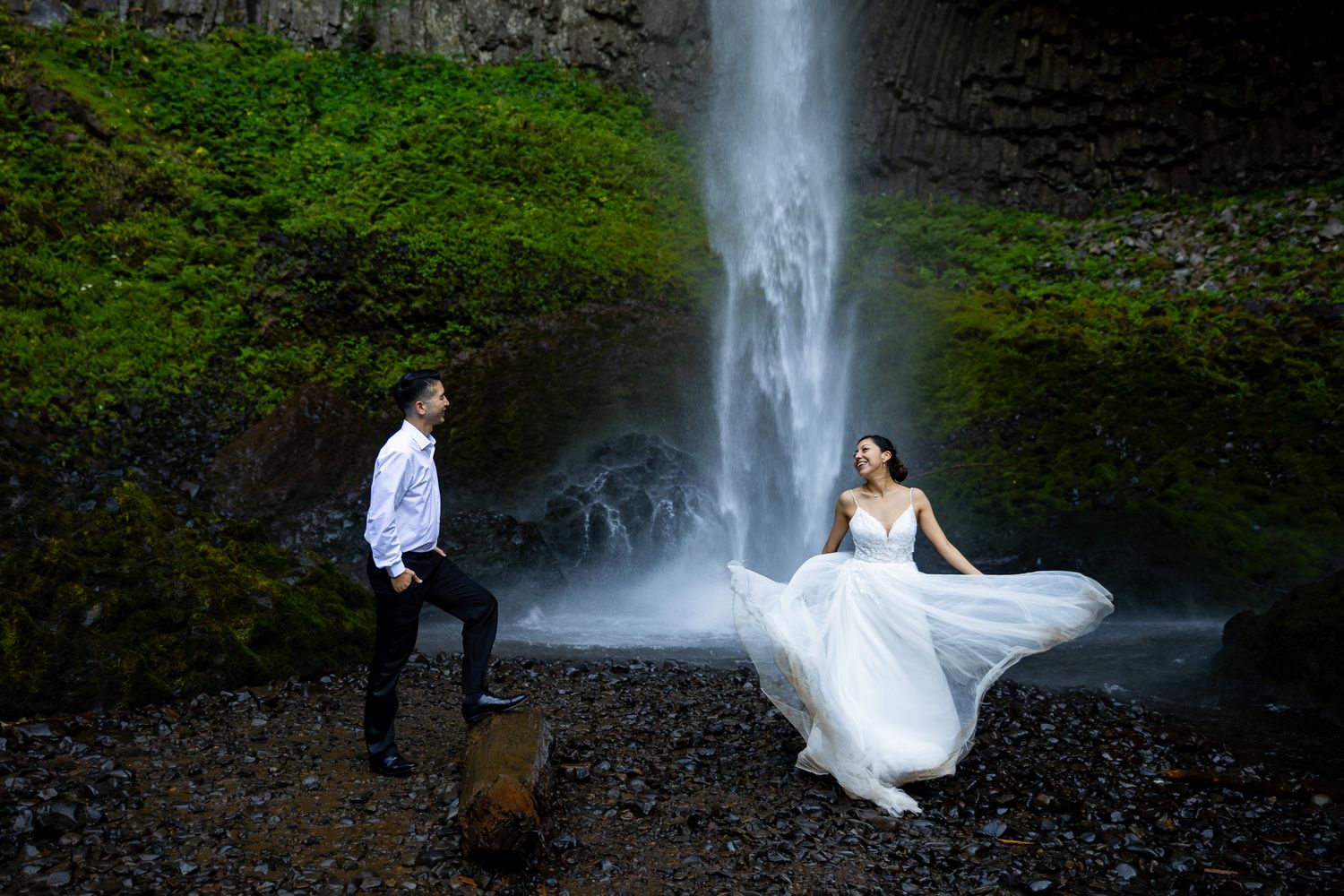 Bride in flowing white gown and groom pose romantically at Latourell Falls.