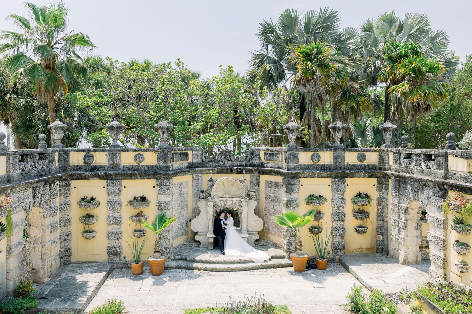 A stone garden terrace with palm trees and potted plants surrounds an ornate fountain at Vizcaya Museum in Miami.