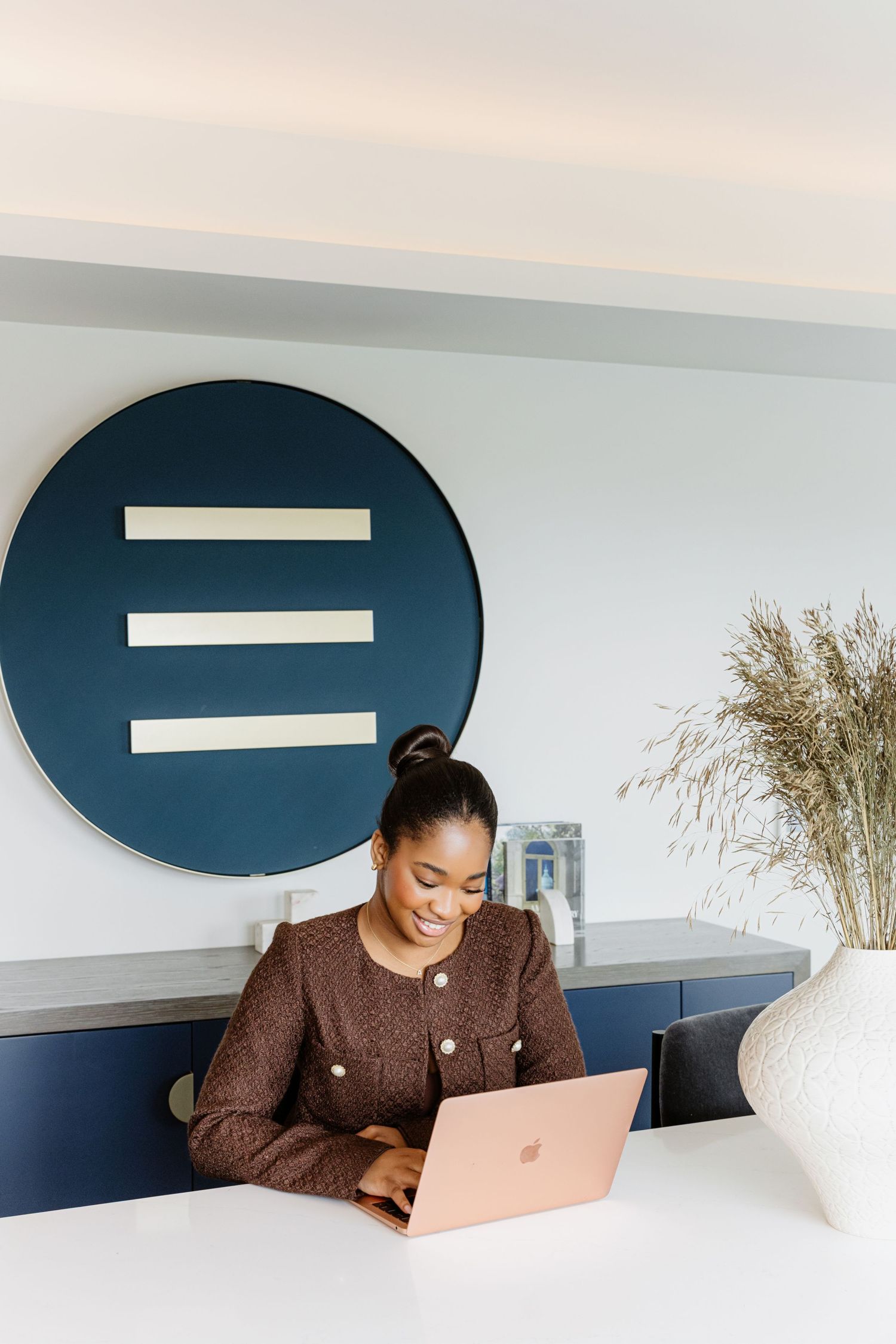 Professional working on laptop in modern office space with navy blue accent wall and minimalist decor.
