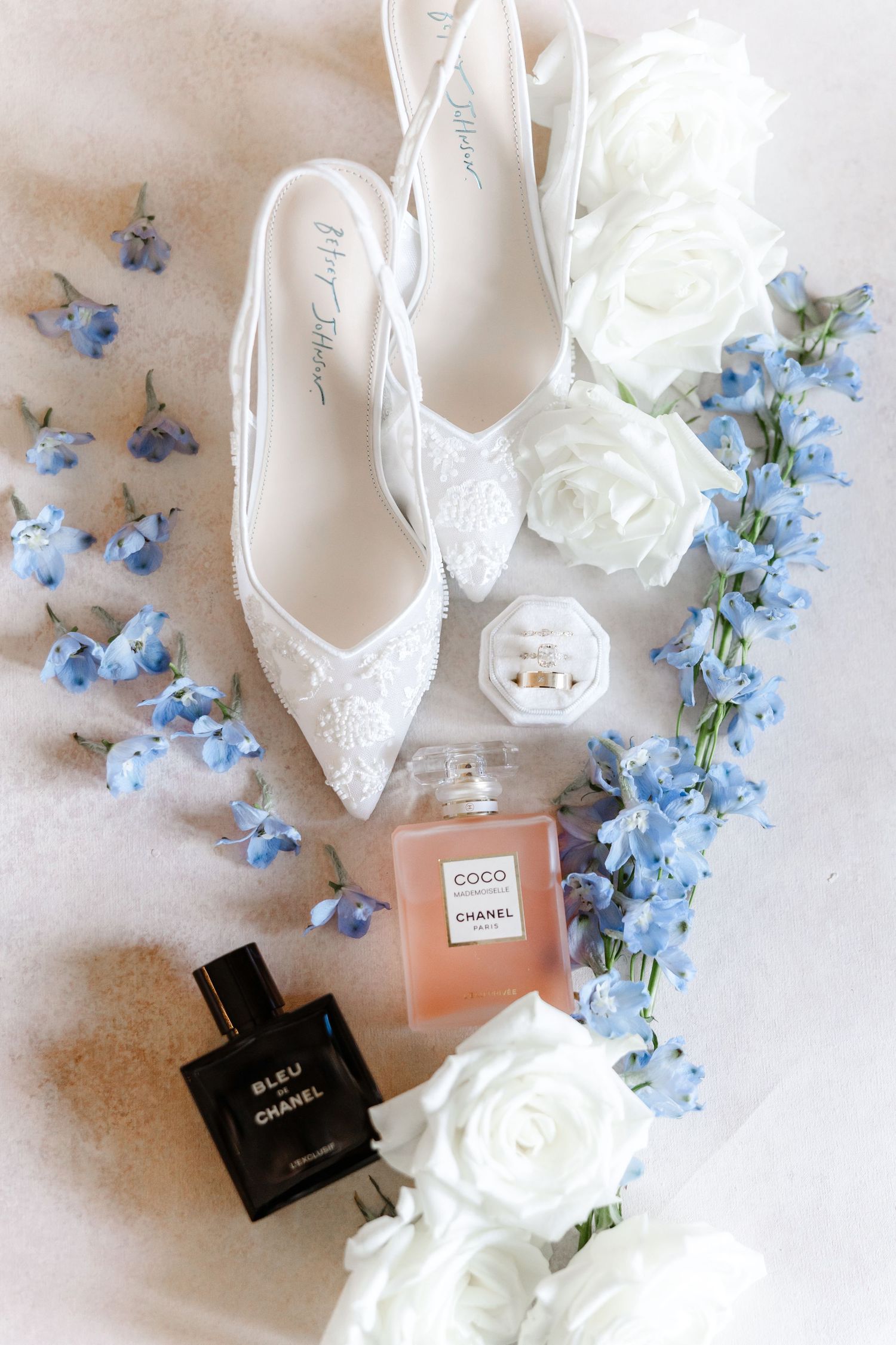 Bridal flat shoes with Chanel Coco and Bleu perfumes, white roses, and blue flowers arranged elegantly.