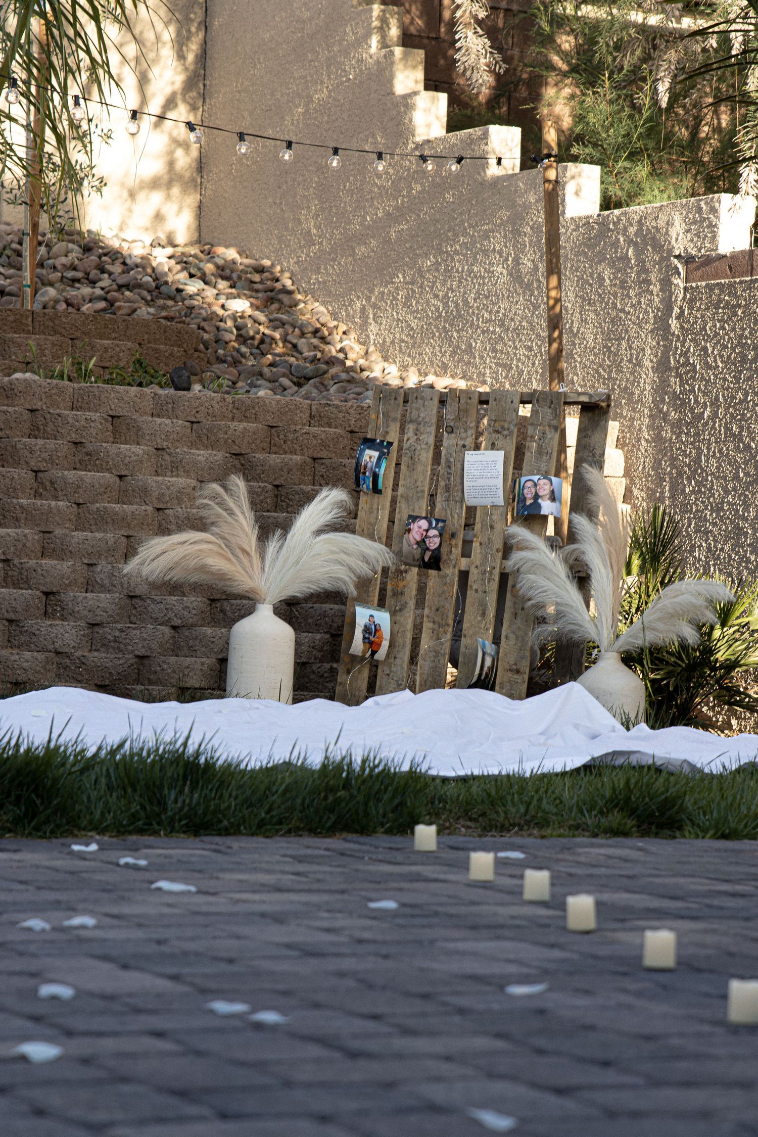Cora Emilie Media Outdoor garden decorated with string lights and white feather arrangements against stone wall.