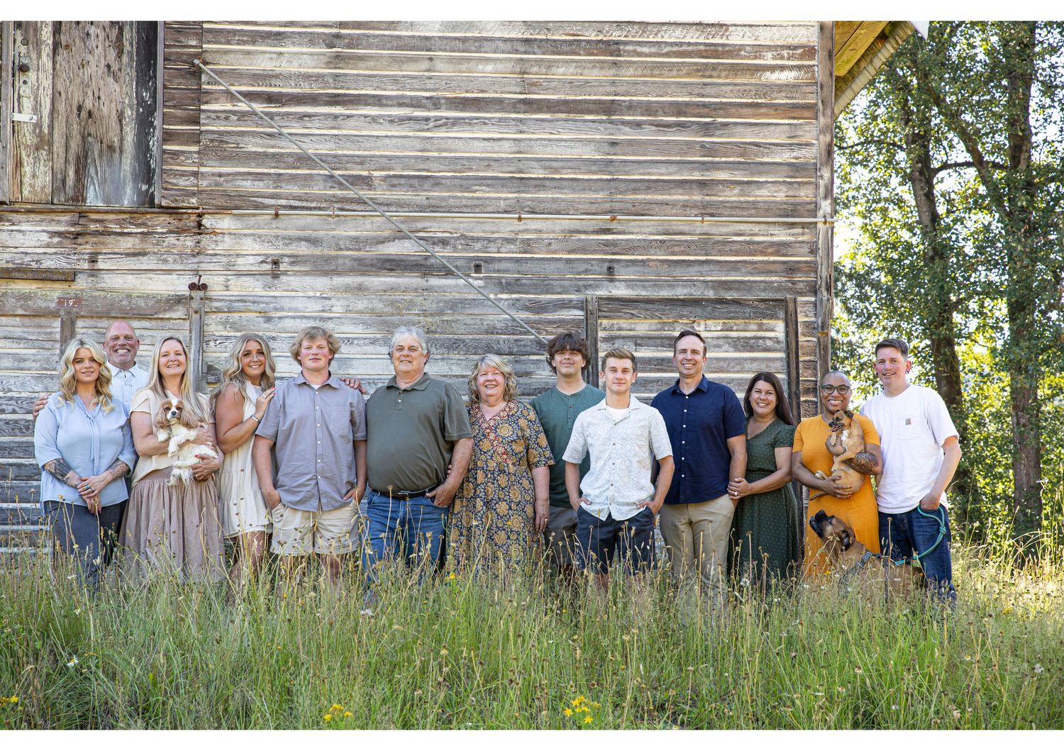 Group photo of people standing together in a row by a rustic wooden barn wall in tall summer grass.