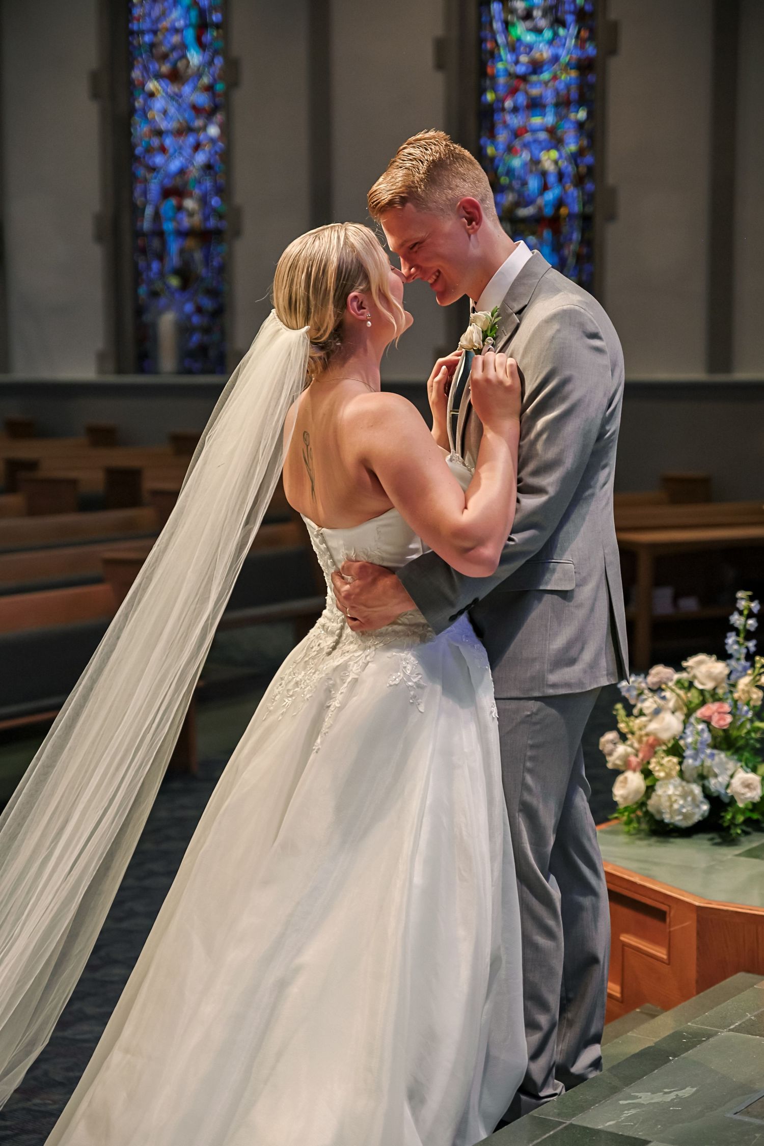 A bride and groom share their first kiss during their wedding ceremony in a church with stained glass windows.
