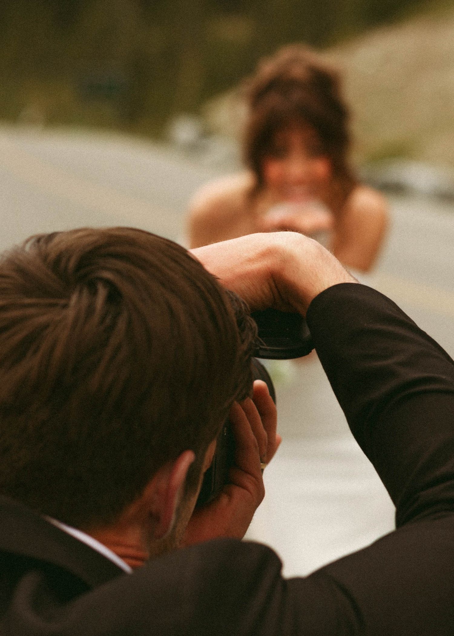 Professional photographer in a black suit takes photos during a photoshoot outdoors.