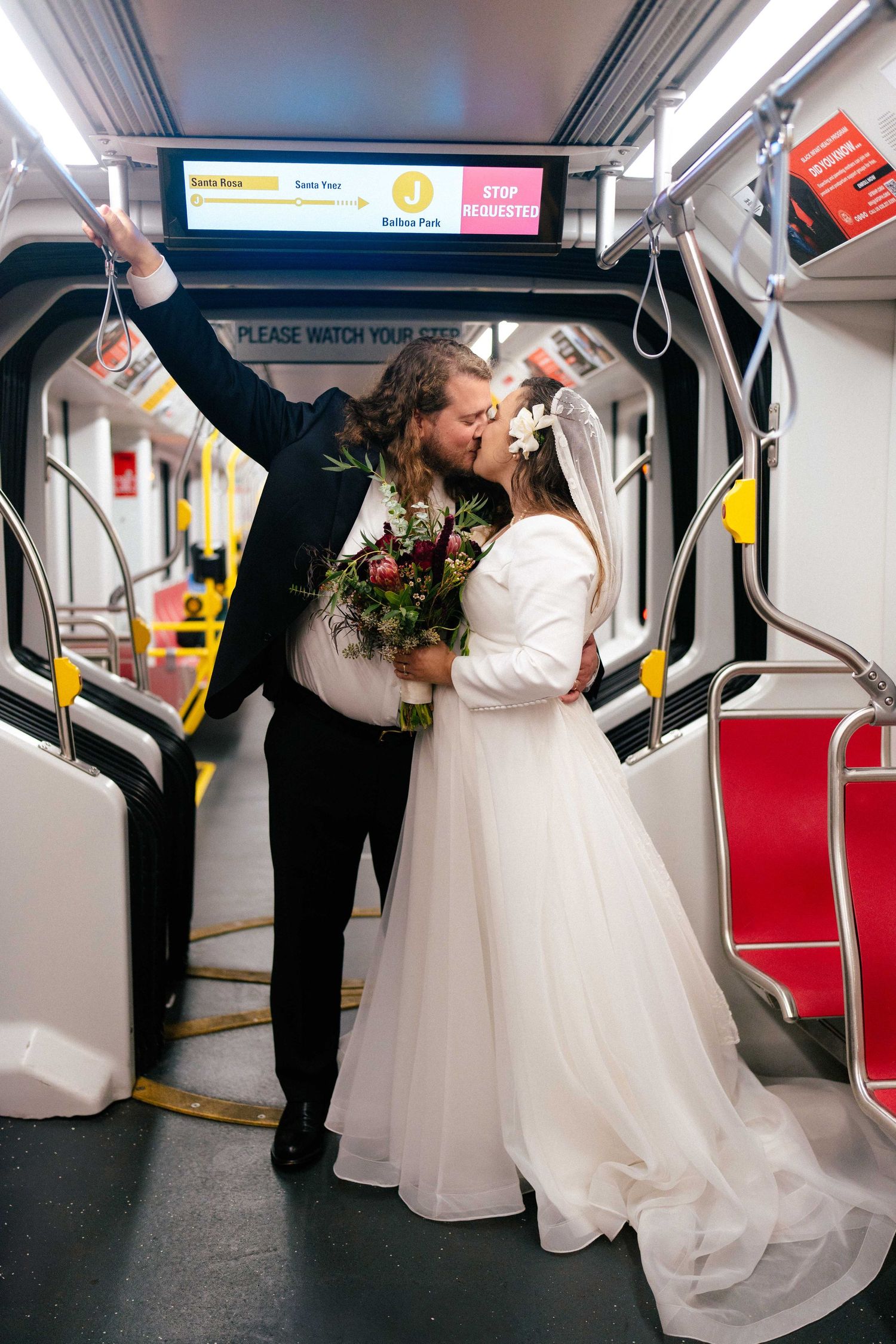 Romantic wedding photo of couple sharing intimate moment on subway train with bouquet.