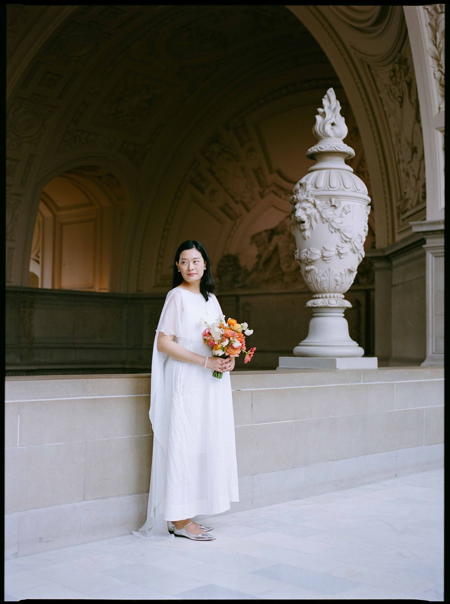 Someone in a white dress holding a bouquet stands on the Fourth Floor of San Francisco City Hall.
