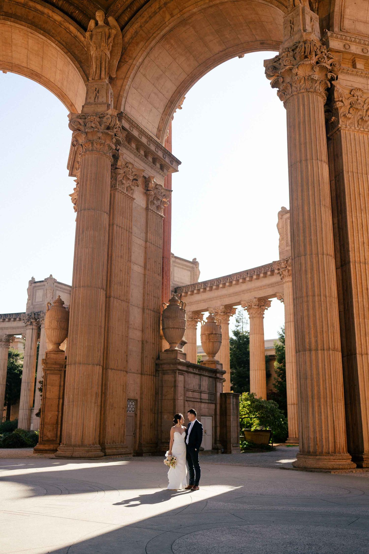 A couple stands beneath grand stone archways at the Palace of Fine Arts in San Francisco during golden hour.