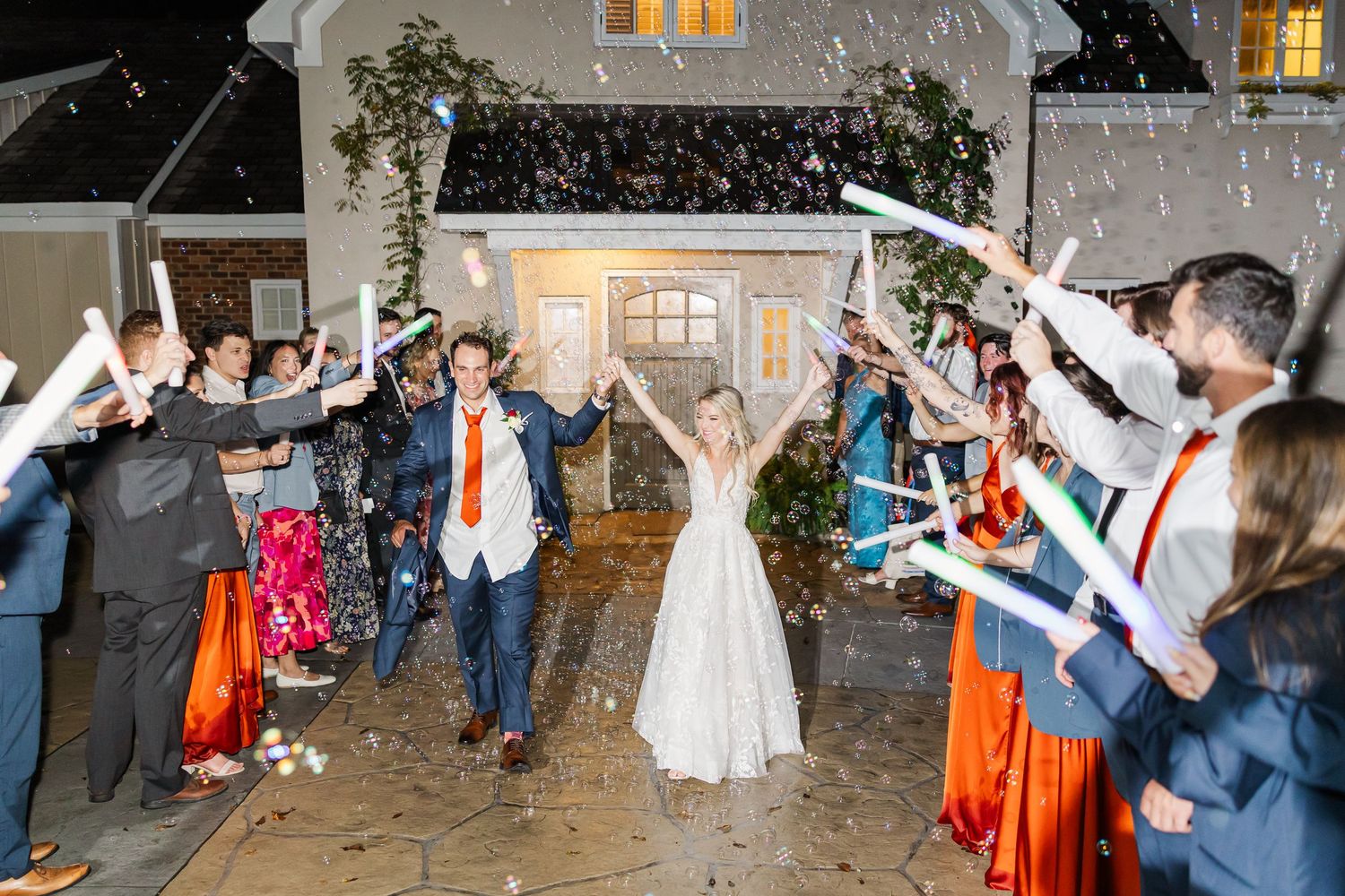 Wedding party celebrates outdoors at night with sparklers creating a magical exit tunnel.