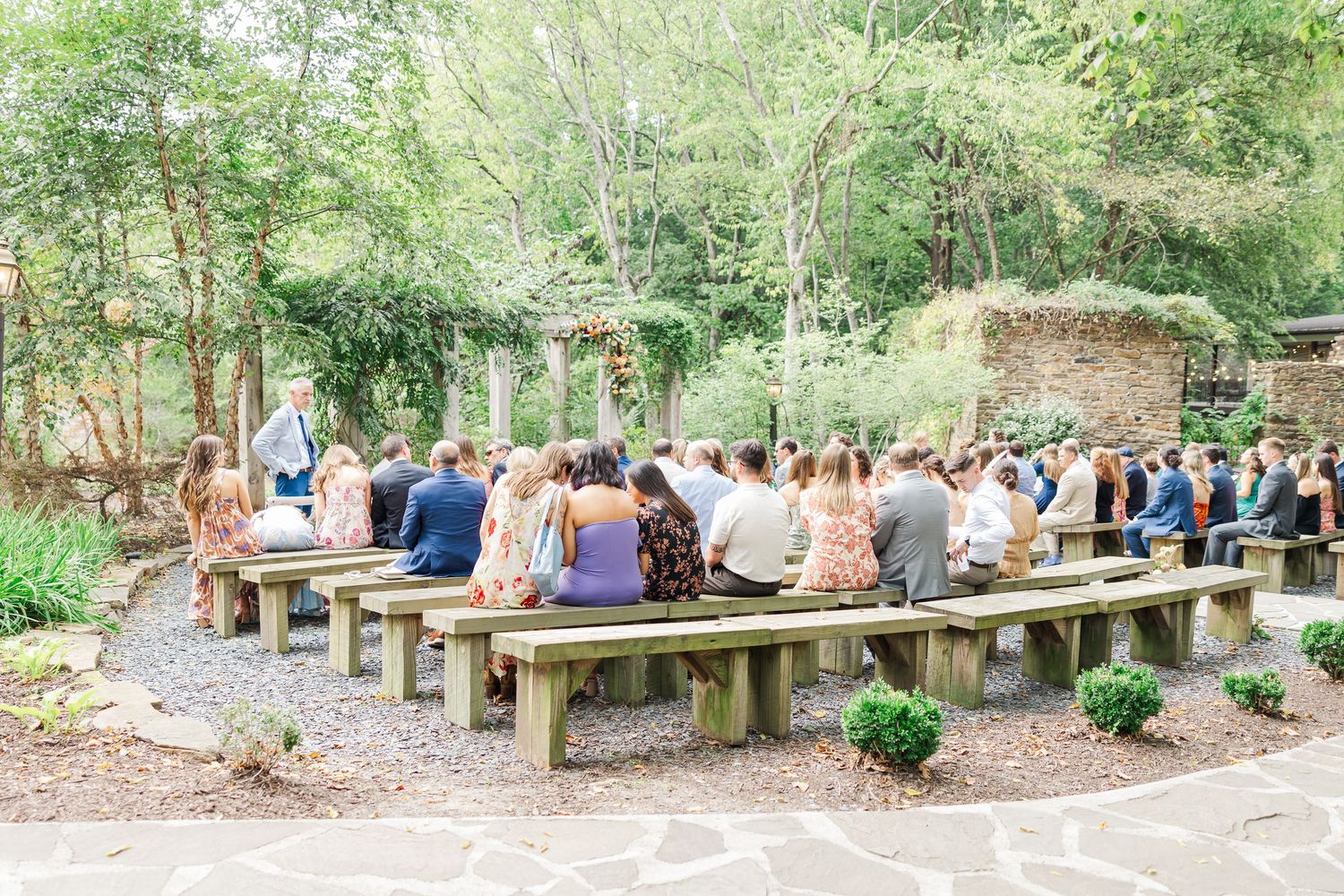 People gather on wooden benches in a tranquil forest setting for an outdoor learning or meeting experience.