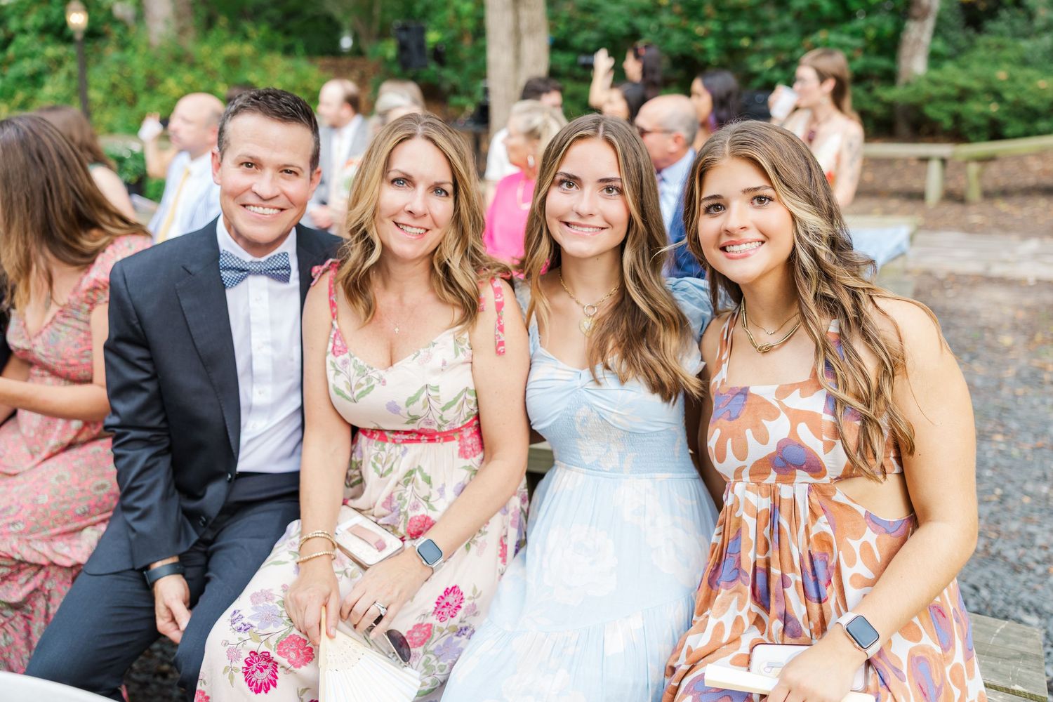 Wedding party members smile and pose together during outdoor celebration in garden setting.