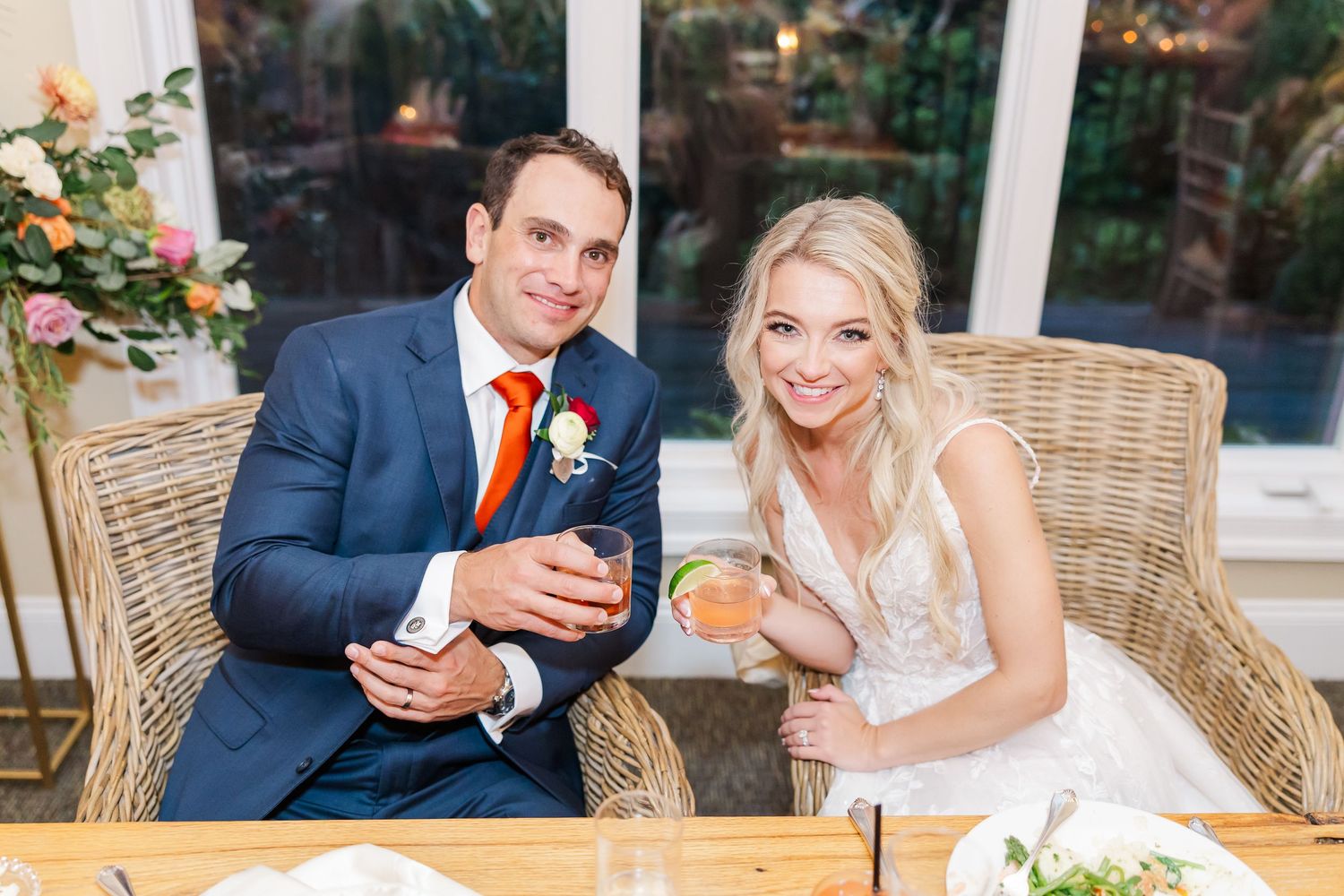 Couple enjoys drinks while seated in wicker chairs at their wedding reception.
