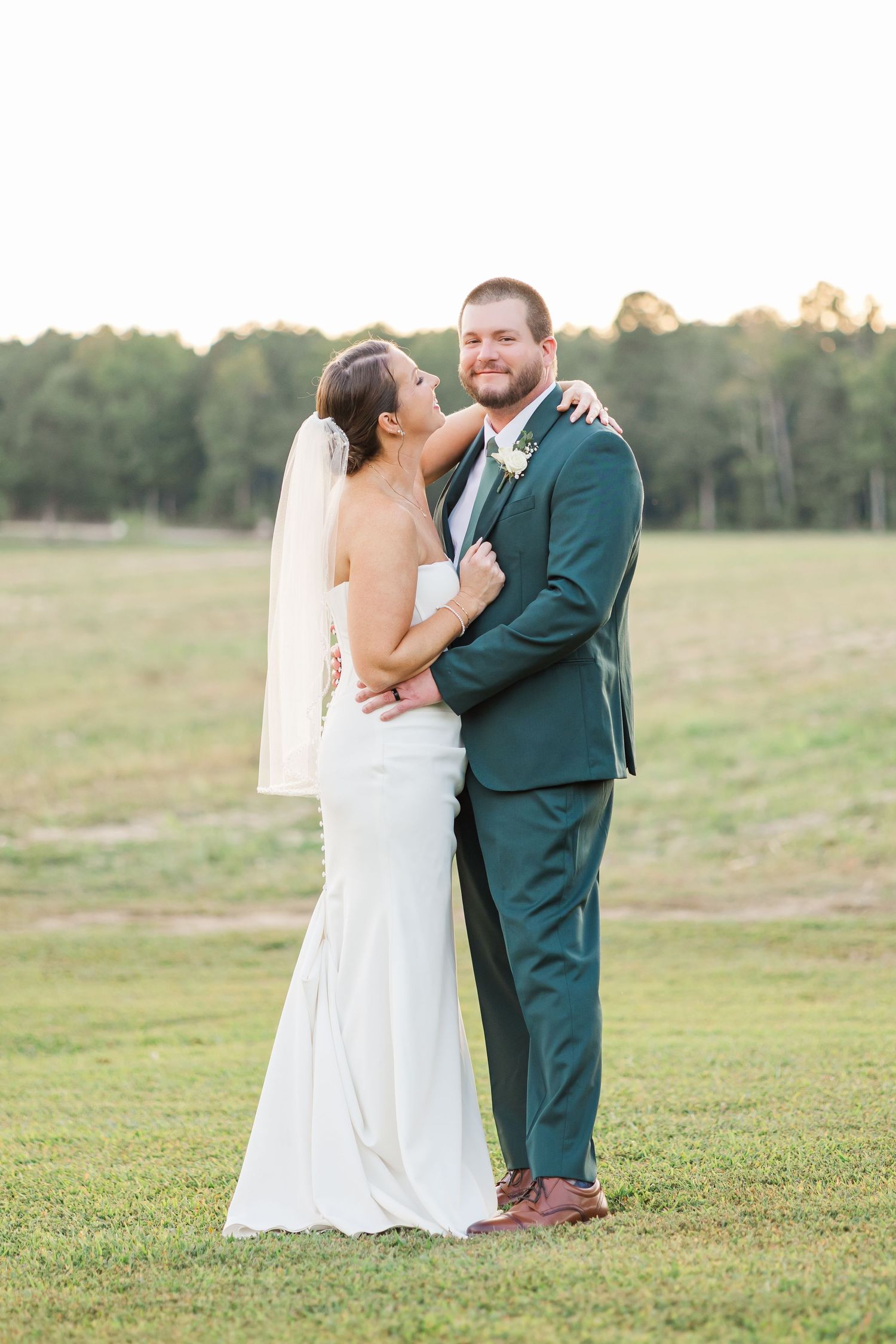 A tender moment between newlyweds on a grassy field during golden hour.