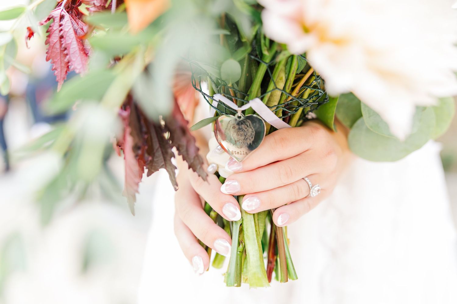 Close-up view of hands holding a fresh floral bouquet with pink and white flowers against a light background.