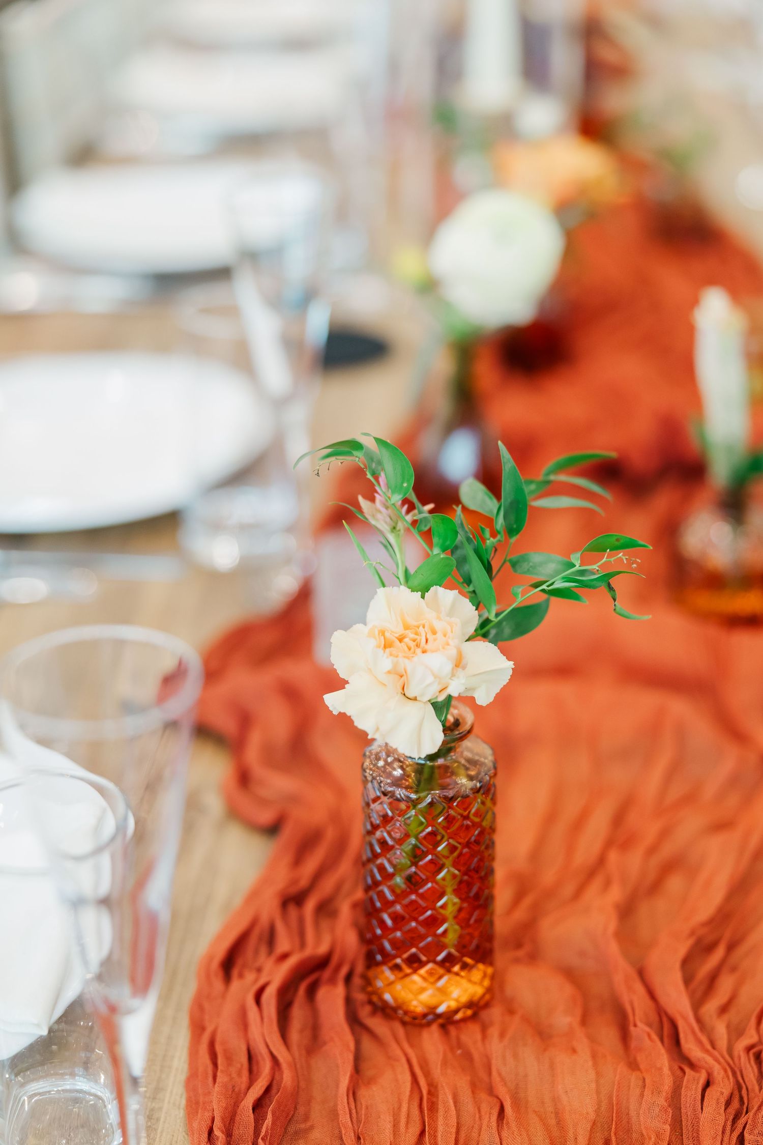 Rustic orange table decor with small floral arrangements in amber glass vases.