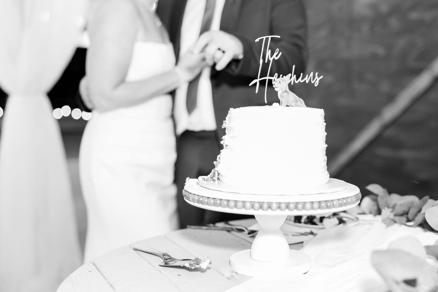 Bride and groom cutting elegant white wedding cake with The Hopkins cake topper at reception.