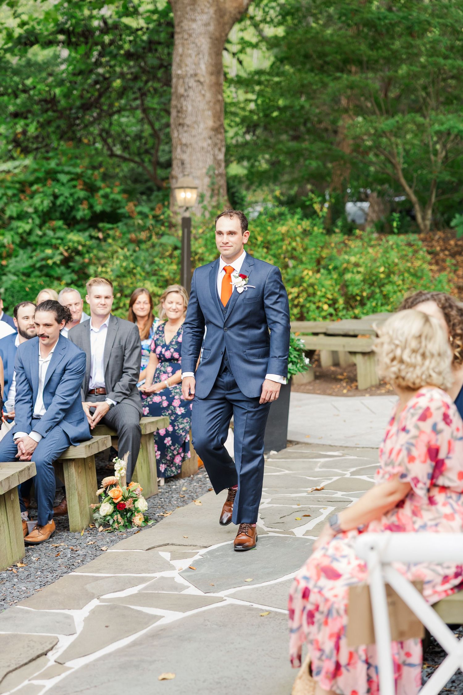 Groomsmen in navy suits play hopscotch on stone pavers in a garden setting.