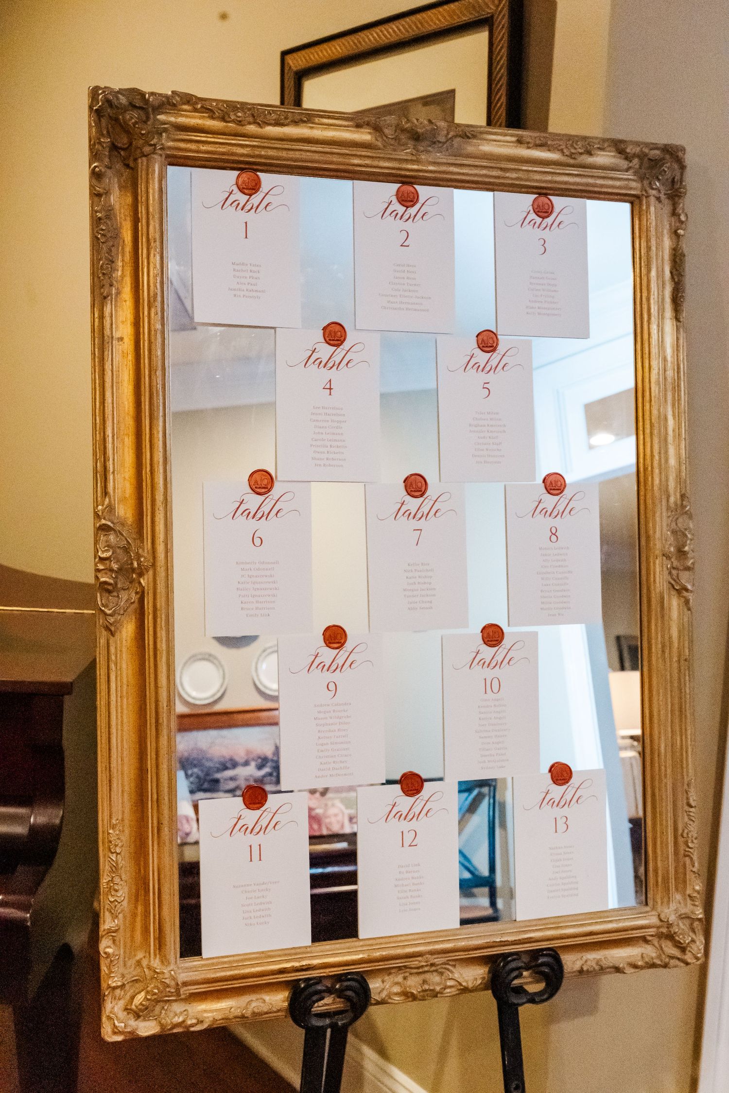 Gold-framed mirror displays wedding seating chart cards with red wax seals.