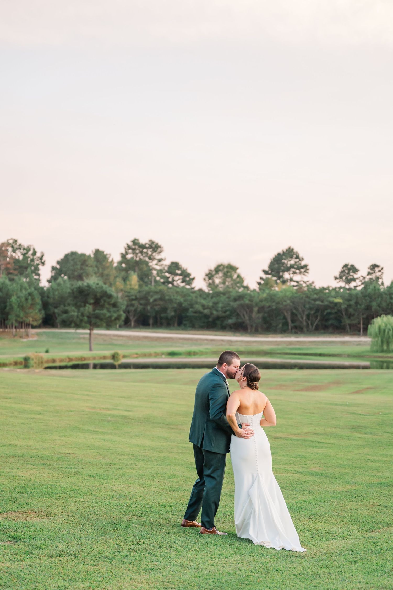 A couple in wedding attire shares an intimate moment on a lush green golf course during golden hour.